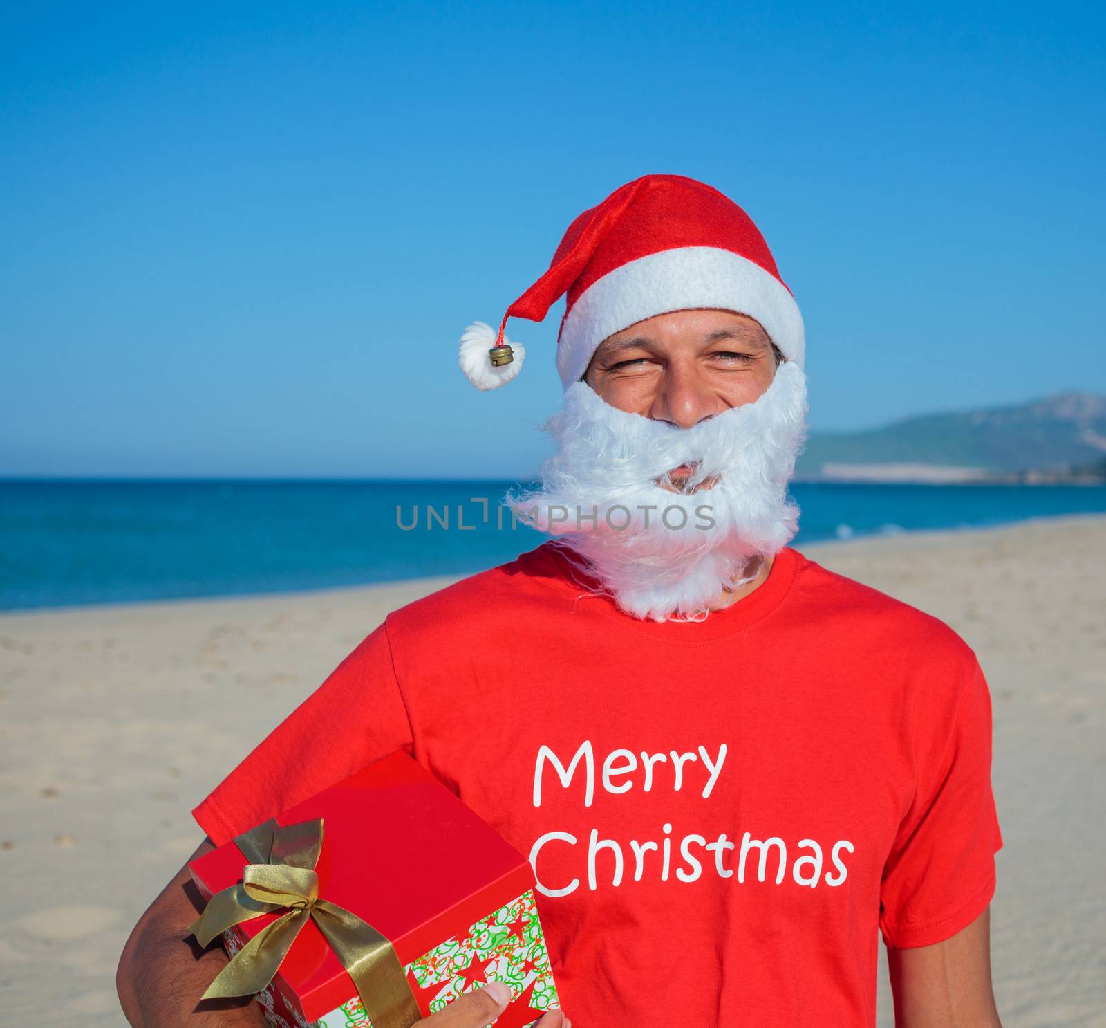 Portrait of young men in Santa hat with gift on tropical vacation