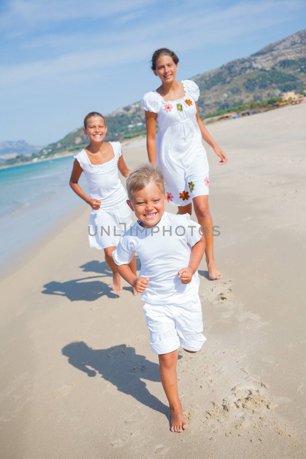 Adorable happy boy with his sisters running on beach vacation