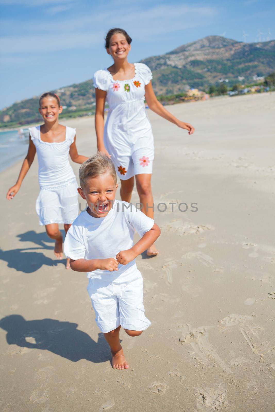 Adorable happy boy with his sisters running on beach vacation