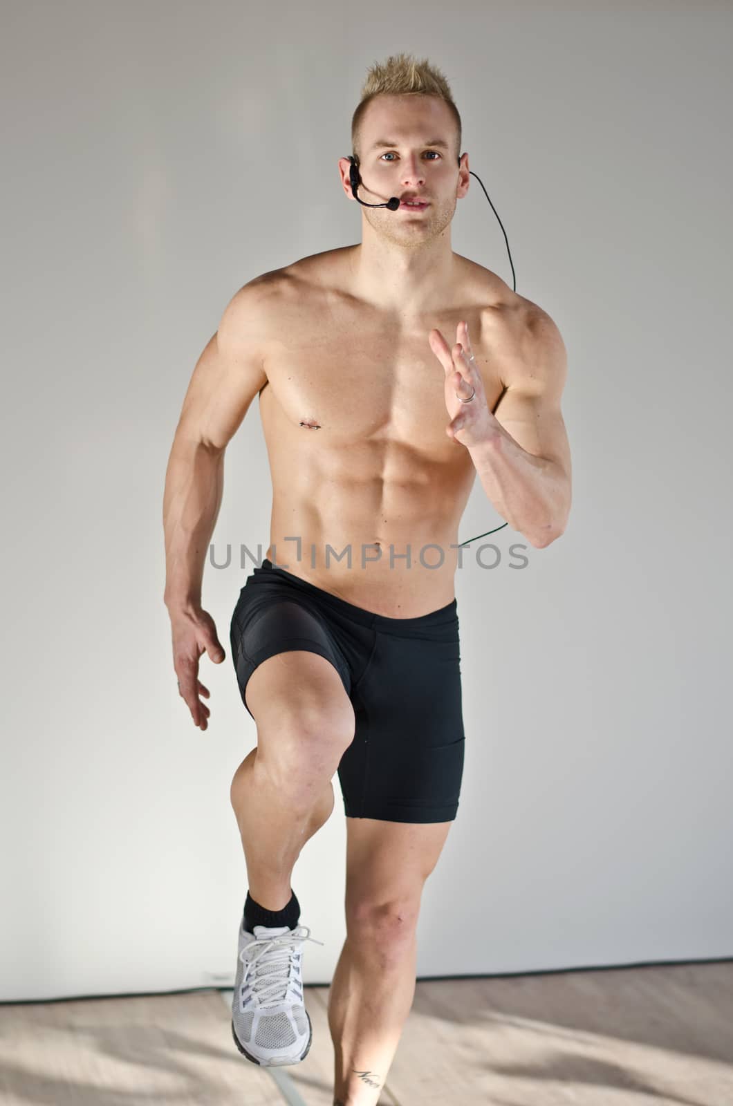Young aerobics male coach shirtless teaching class, standing with headset on