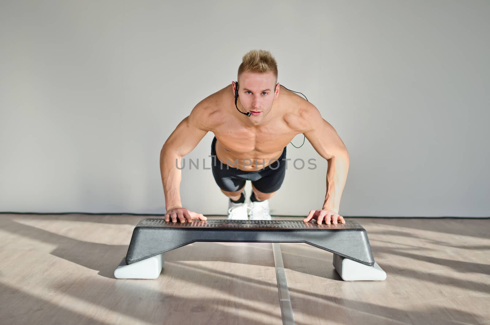Young aerobics male coach shirtless leaning on step teaching class