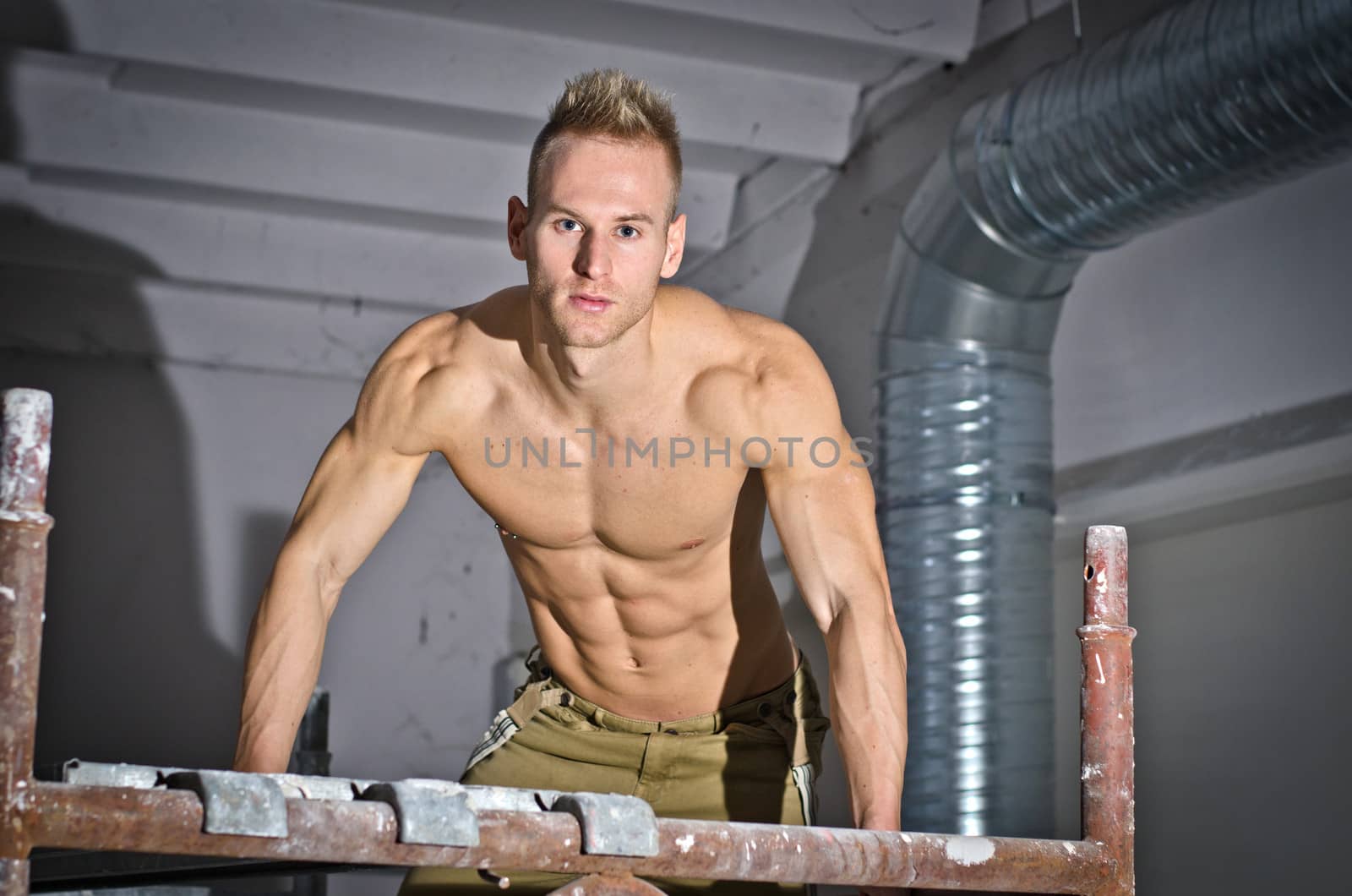 Handsome, muscular young construction worker climbing scaffolding, looking at camera