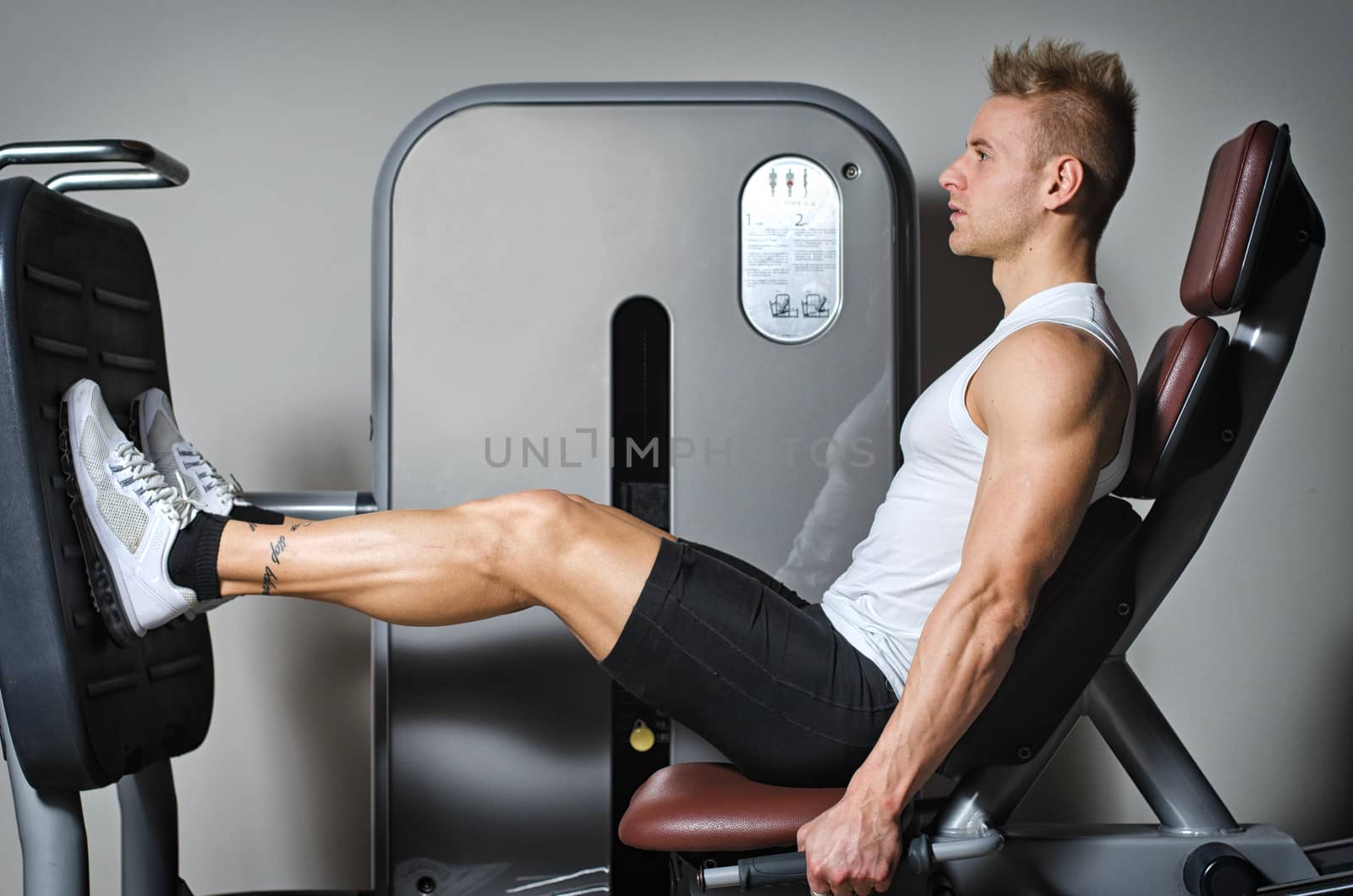 Attractive and fit young man in gym working out legs and exercising on equipment