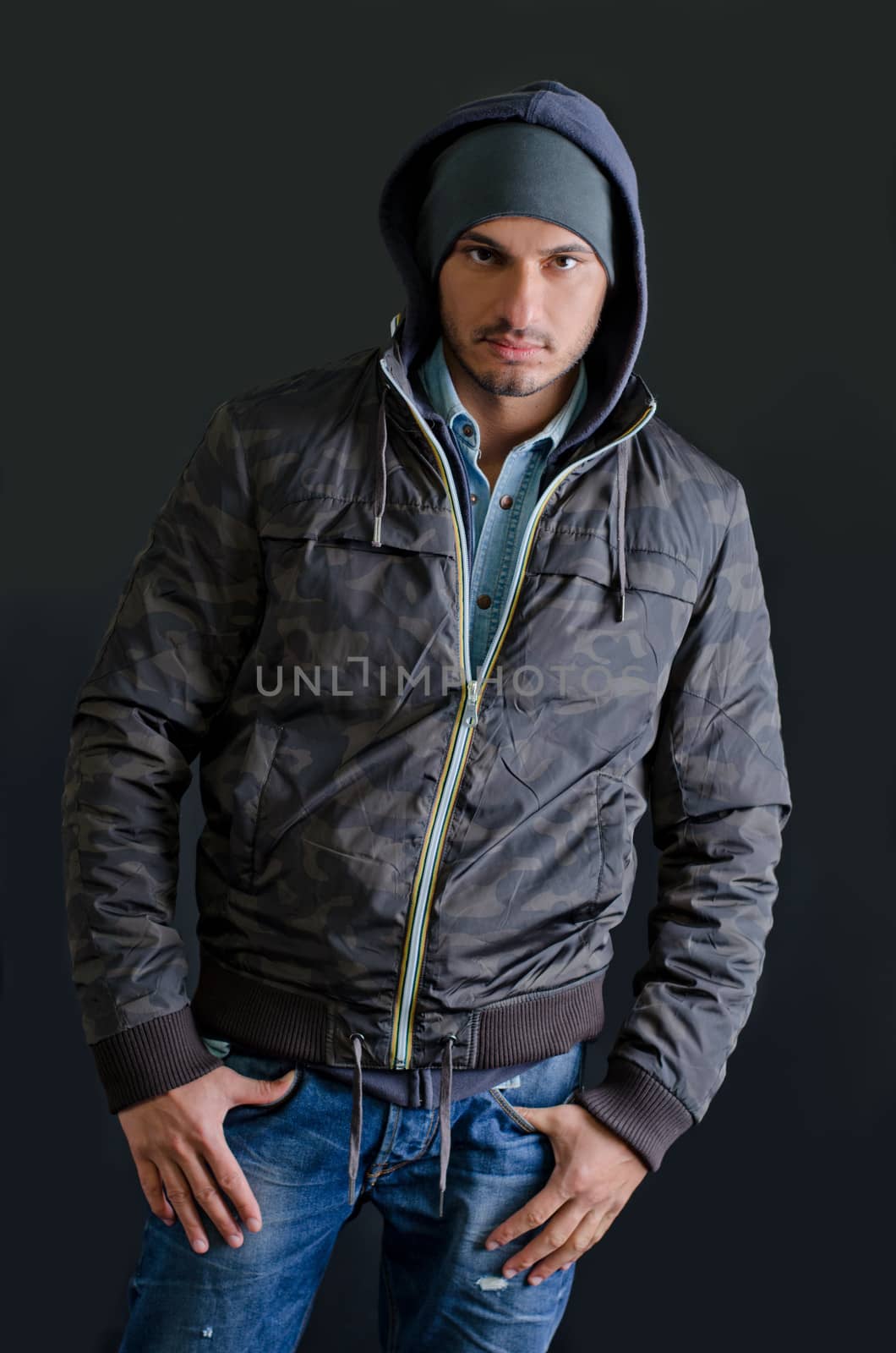 Trendy young man in winter clothes, jeans and hoodie, studio shot on dark background