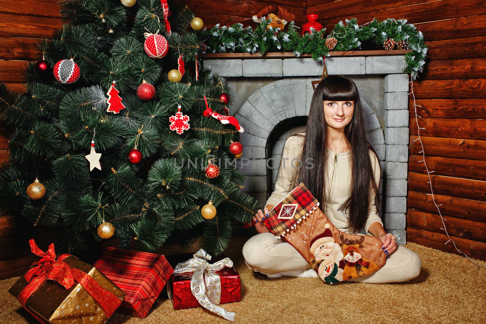 Attractive young woman holding gift and sits near Christmas tree