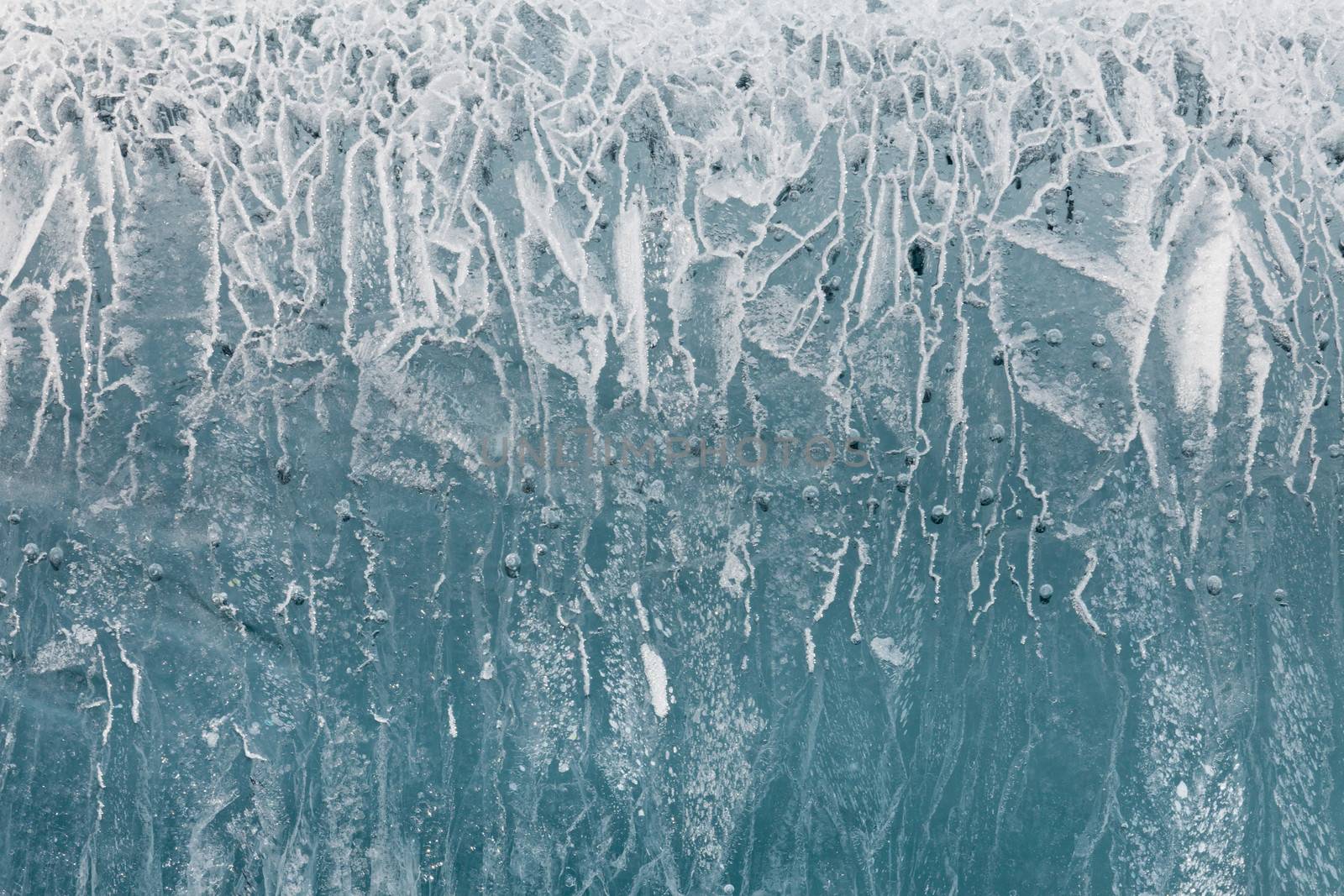 Weathered frozen water ice surface candelized with cracks and air bubbles nature background texture pattern