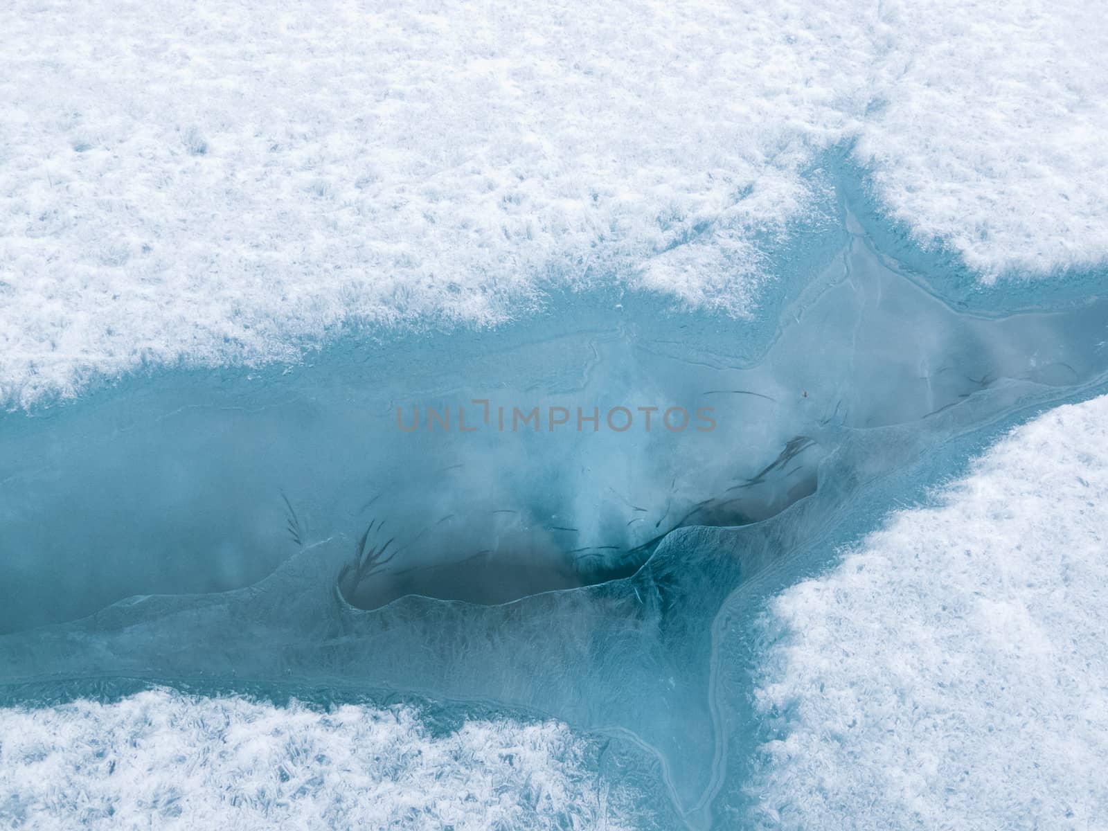 Open water in crack of ice sheet cover of wintery frozen lake in a winter nature background pattern abstract