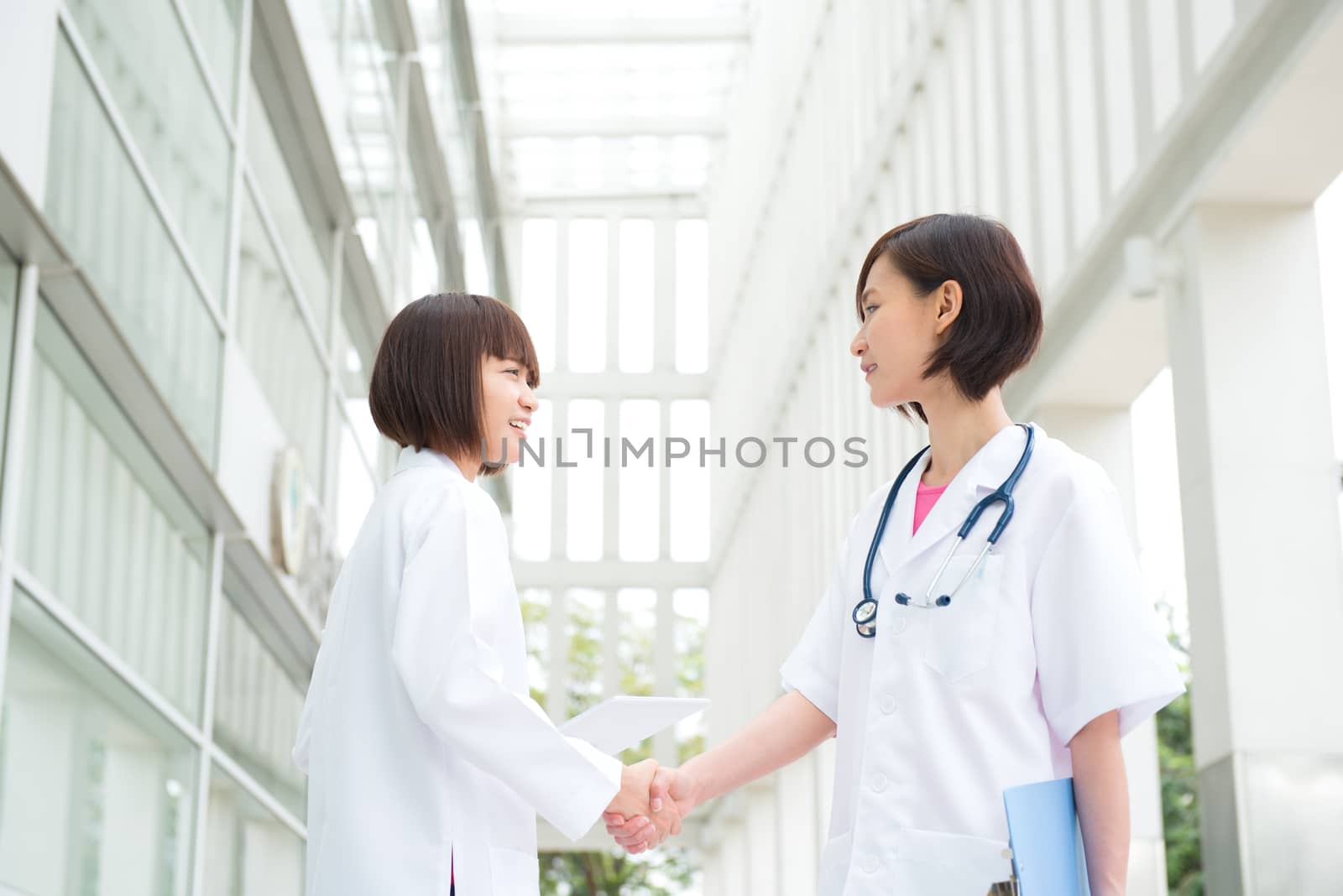 Two Asian medical doctors shaking hands at hospital corridor, teamwork concept.