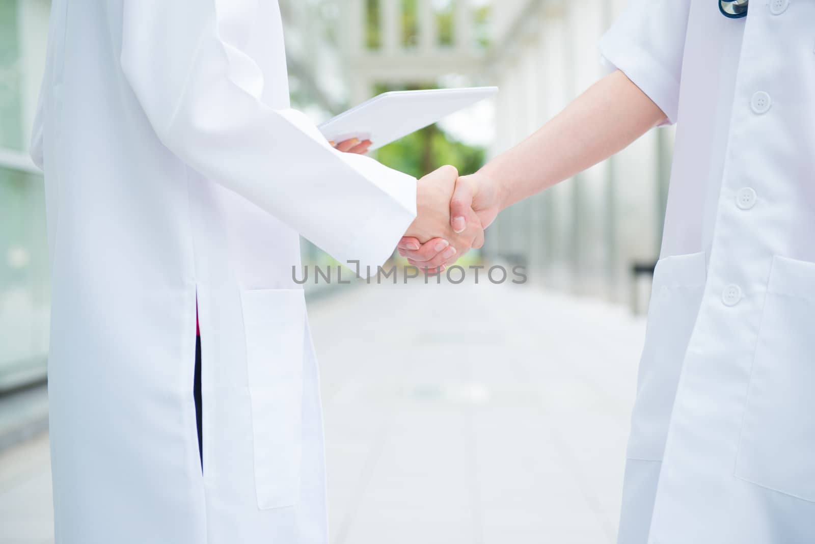 Two medical doctors shaking hands at hospital corridor, teamwork concept.