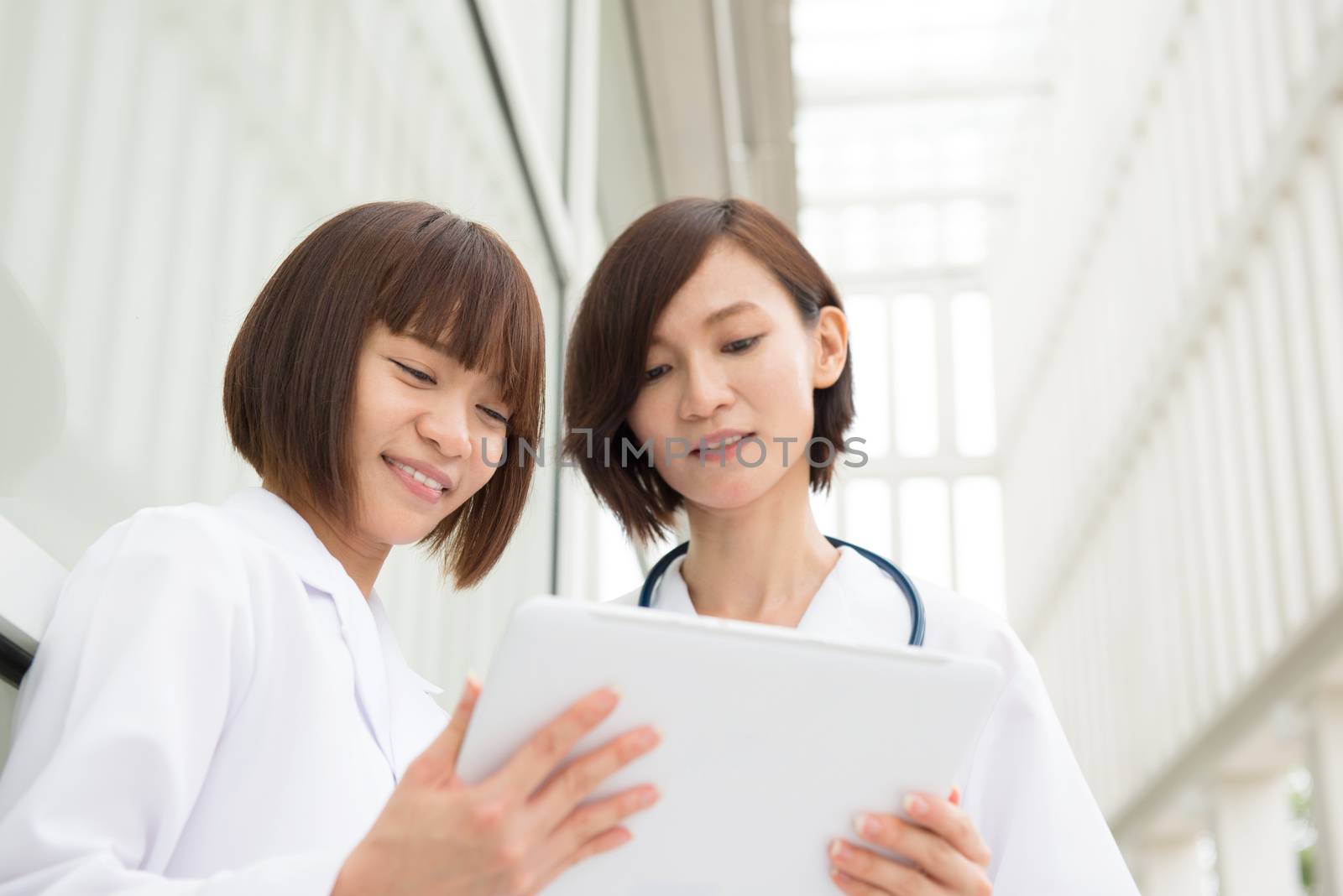 Asian doctors having discussion at hospital corridor. Using digital computer tablet.