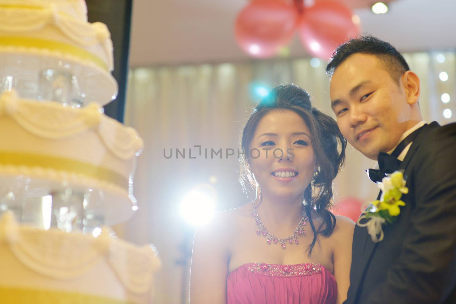 Asian Chinese wedding dinner reception. Bride and groom cake cutting, natural candid photo.