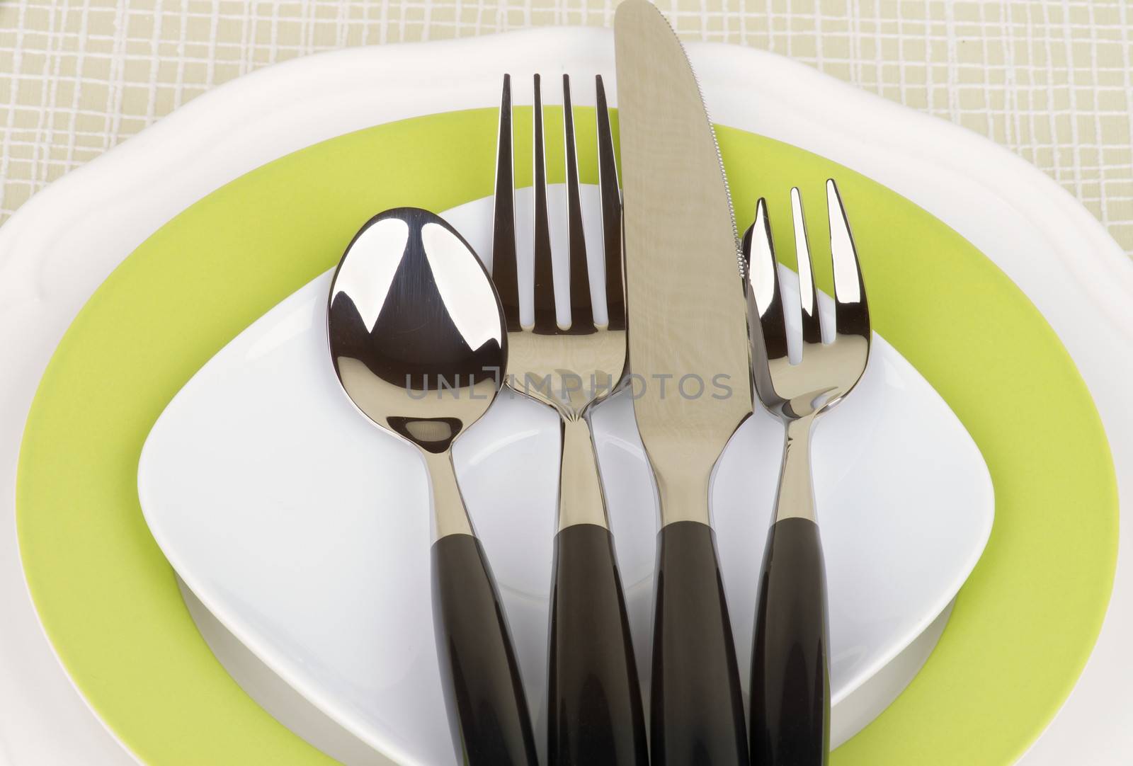 Elegant Table Setting with Spoon, Fork, Table Knife and Dessert Fork on White and Green Plates closeup