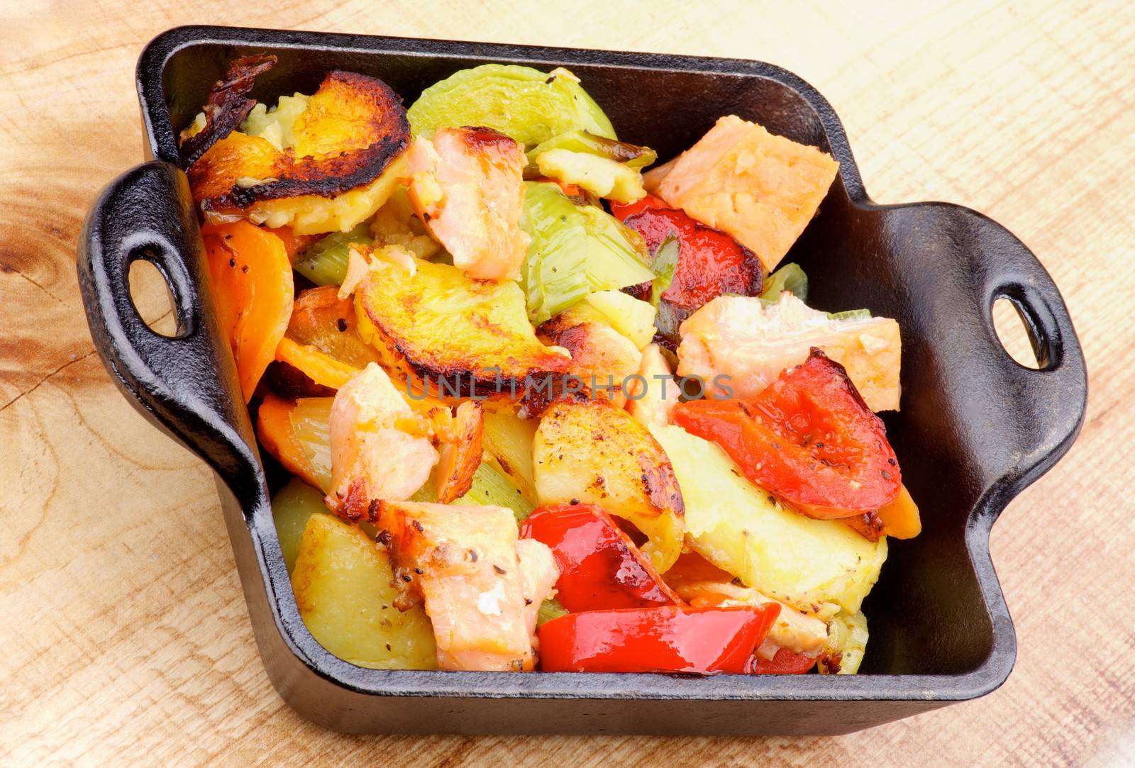 Delicious Homemade Salmon Stew with Potato, Red Bell Pepper, Leek and Carrot in Black Frying Pan closeup on Wooden background