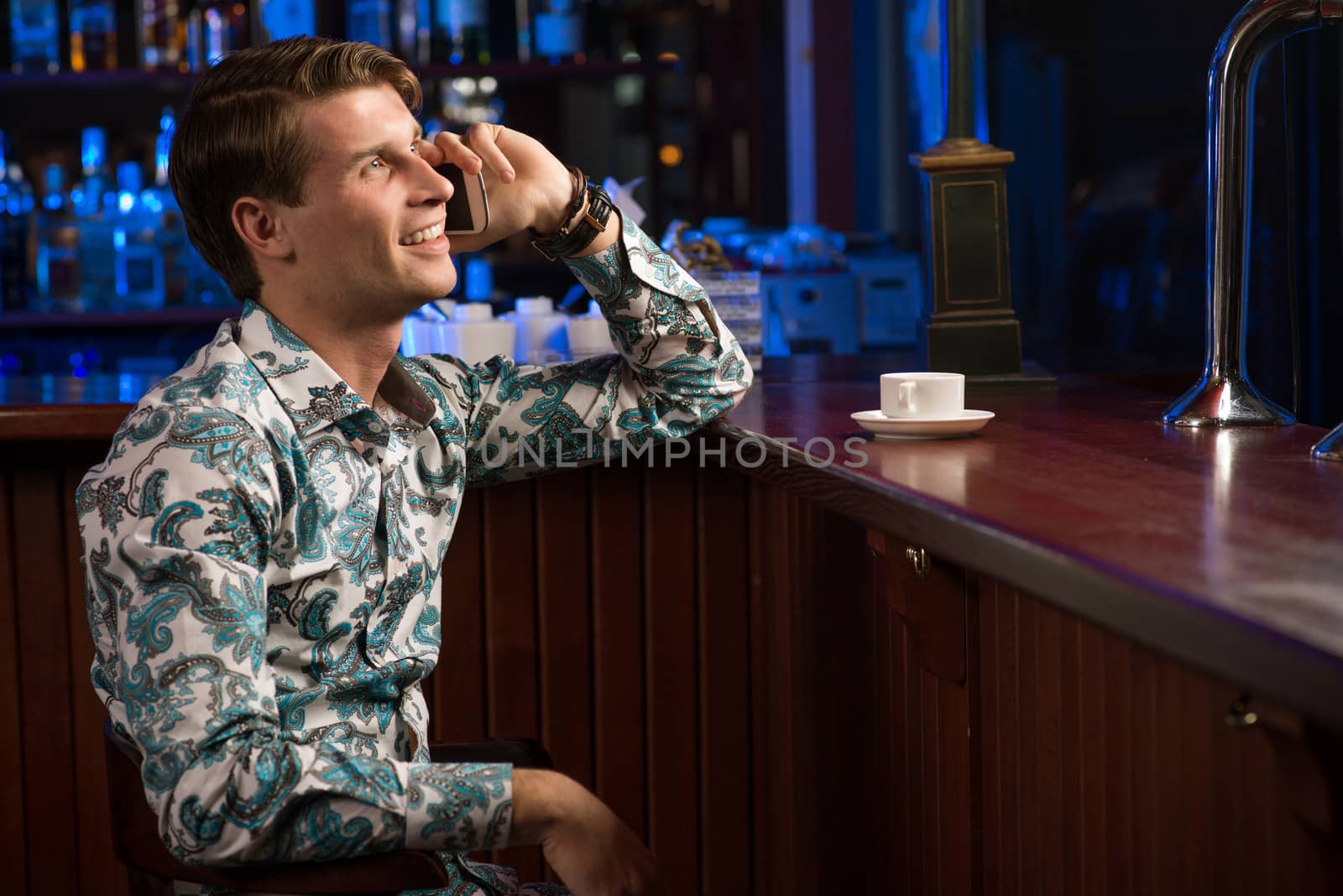man talking on the phone while sitting with a cup of coffee at the bar