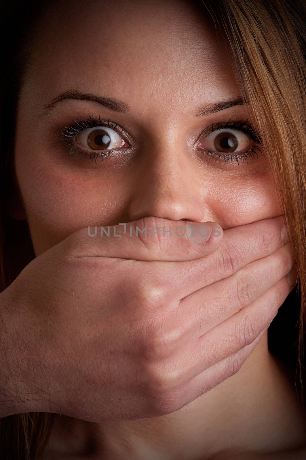 Closeup of a mans hand covering a womans mouth. Concept of domestic violence or kidnapping. Dark mood.
