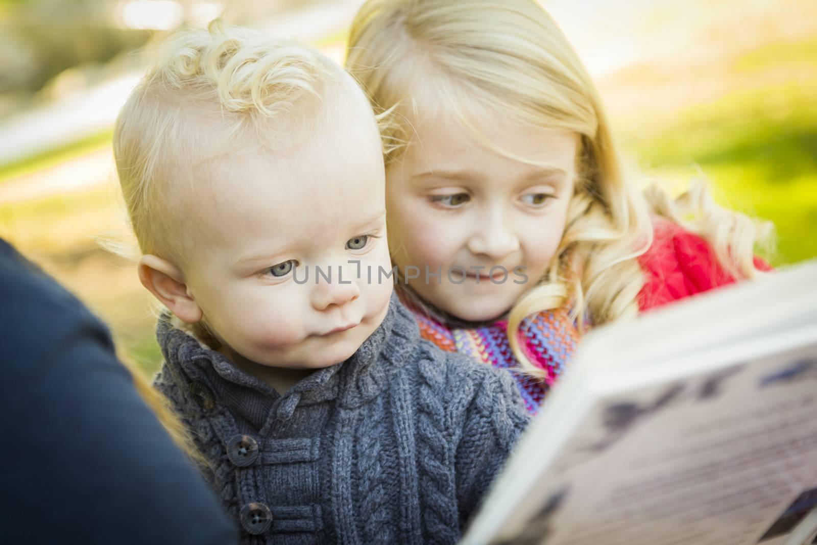Mother Reading a Book to Her Two Adorable Blonde Children Wearing Winter Coats Outdoors.
