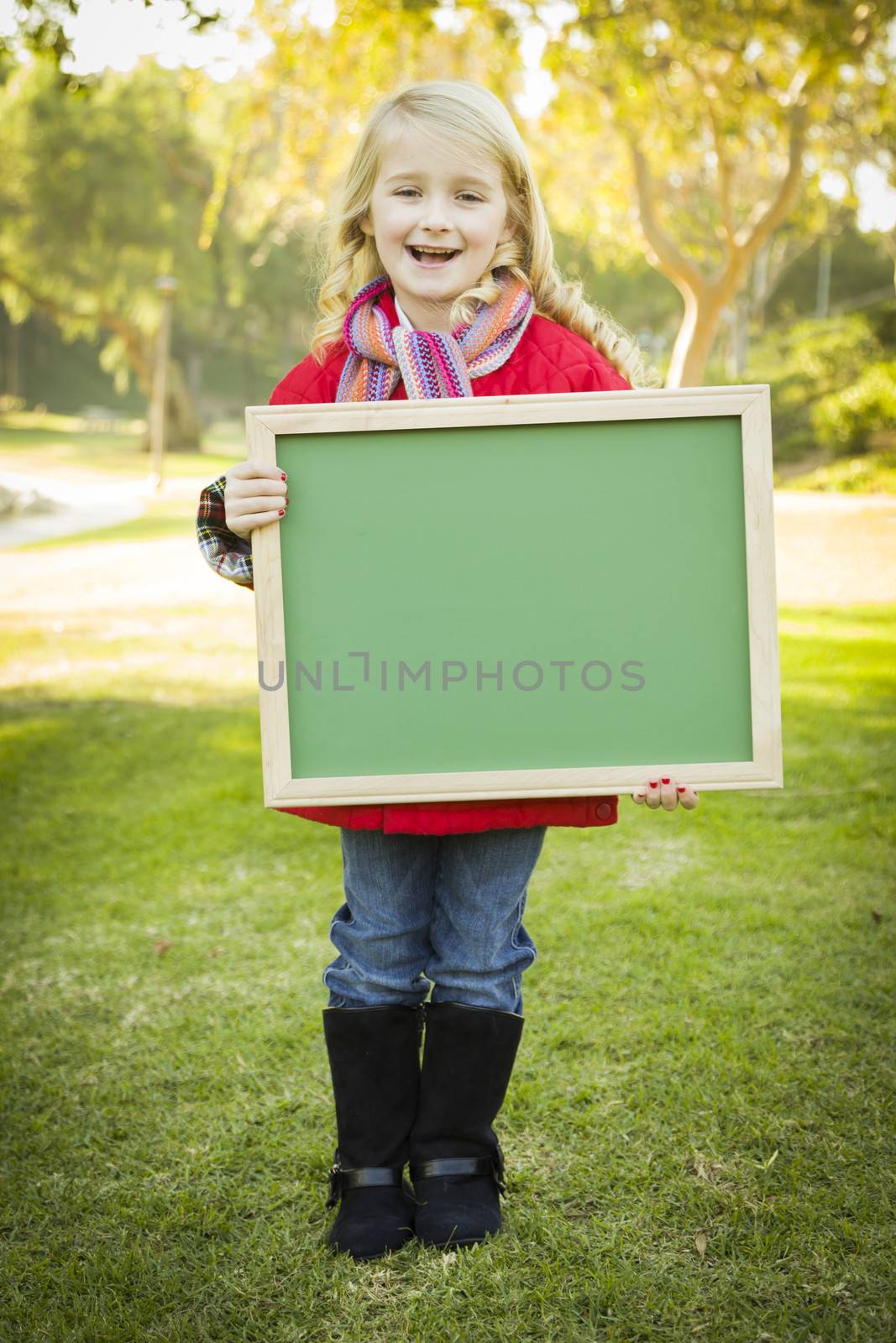 Cute Little Blonde Wearing Winter Coat and Scarf Holding a Green Chalkboard Outdoors.
