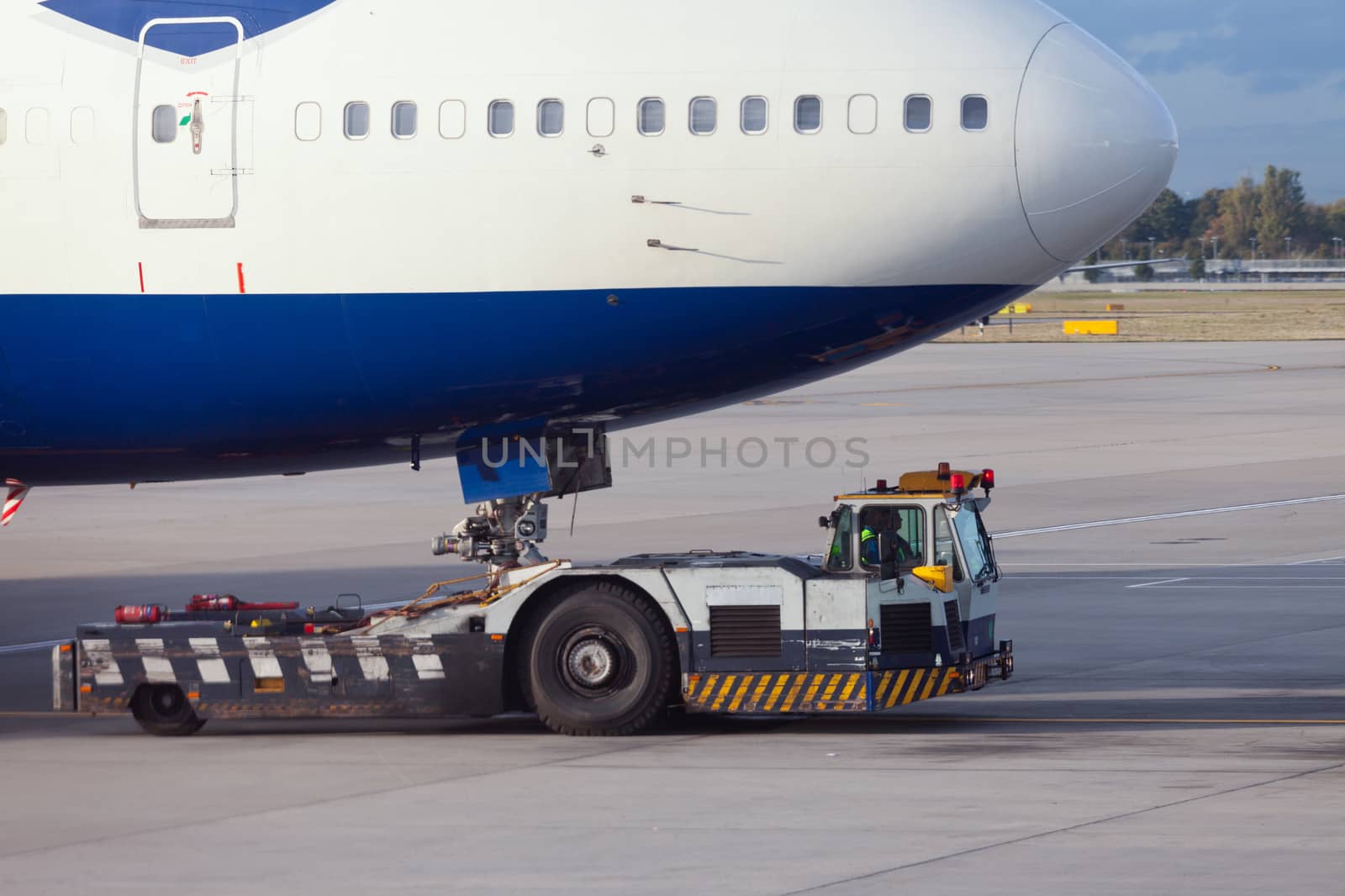 Large aircraft being pulled by airport tug tractor taxing on airfield into docking position for passenger boarding the airplane