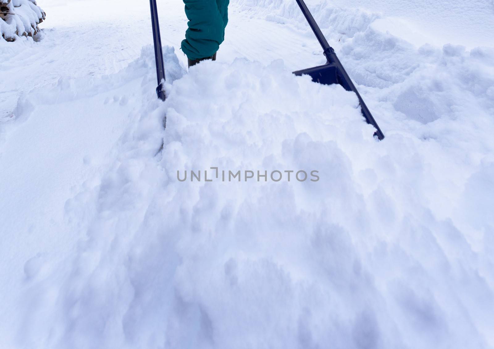 Manual snow removal from driveway using a snow scoop by person wearing boots