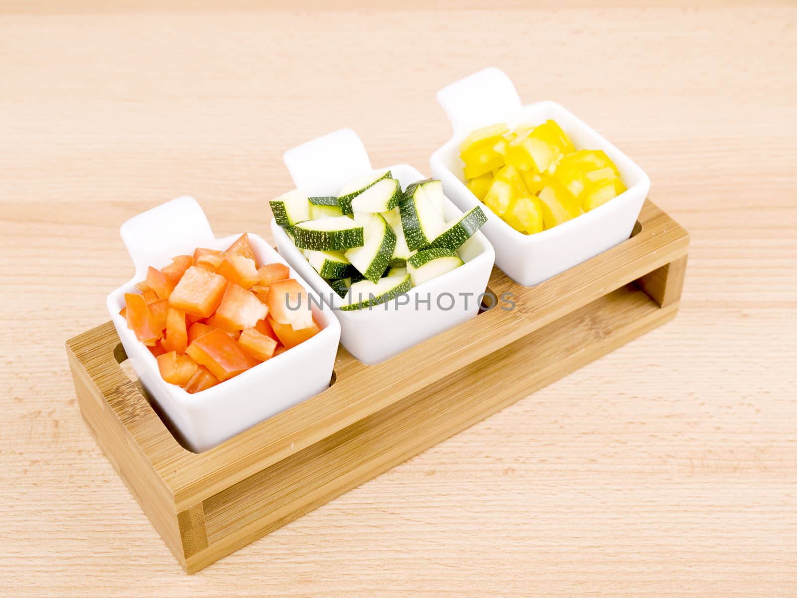 Fresh choped paprika and zucchini in small porcelain bowls on wooden table