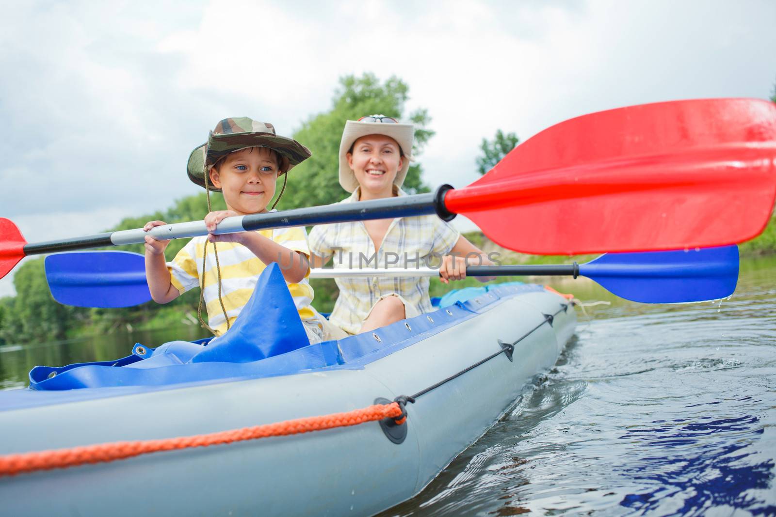 Happy little boy with mother paddling kayak on the river in lovely summer day