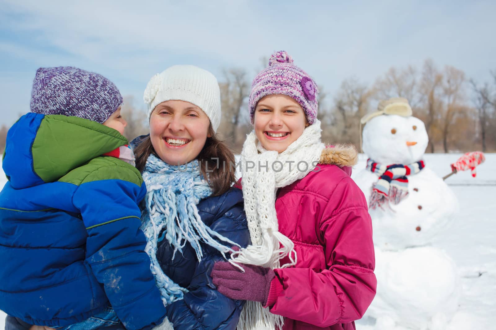 Happy mother with two kids building snowman outside in winter time