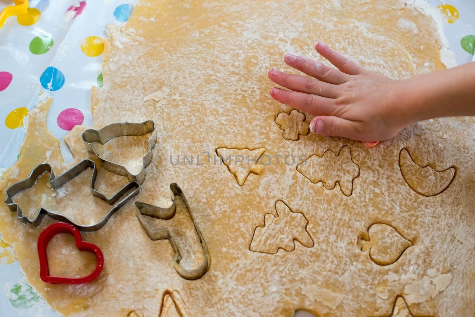 Children baking Christmas cookies: Cutting pastry with a cookie cutter on a colorful table cloth