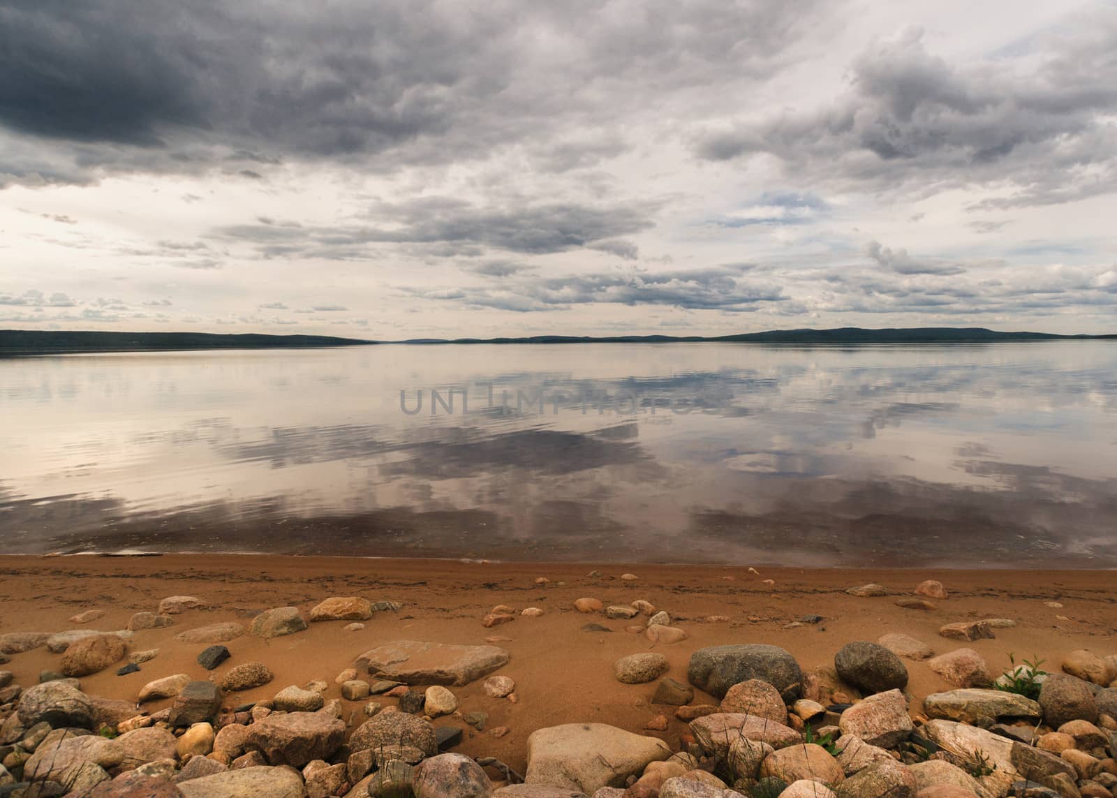 Rocky beach fronts lake reflecting dramatic skies in Lapland. by Claudine