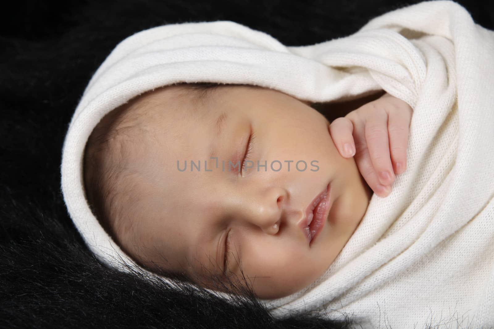 Sleeping baby girl wrapped in cloth against black