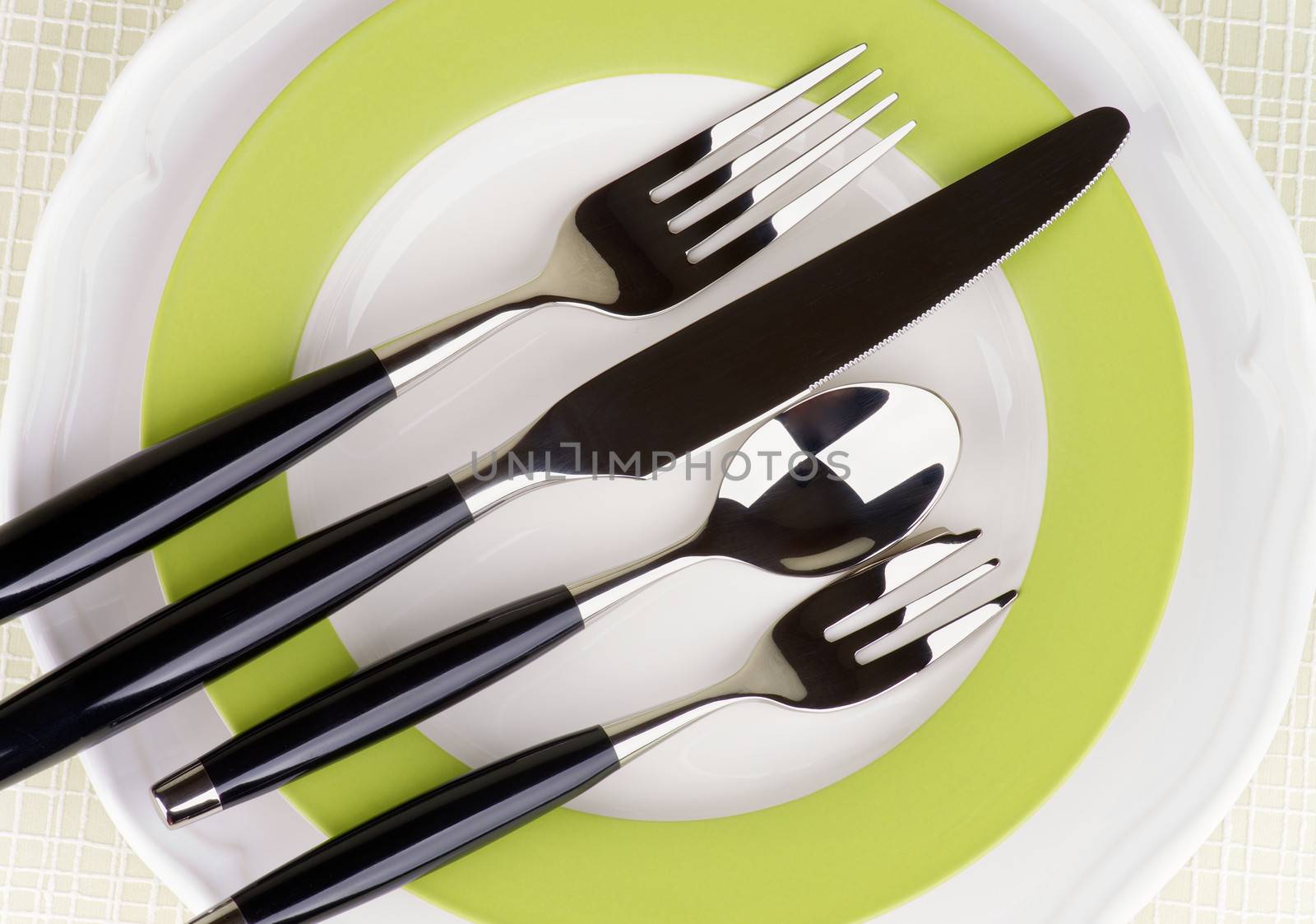 Elegant Table Setting with Fork, Table Knife, Spoon and Dessert Fork with Black Handles on White and Green Plates. Top View