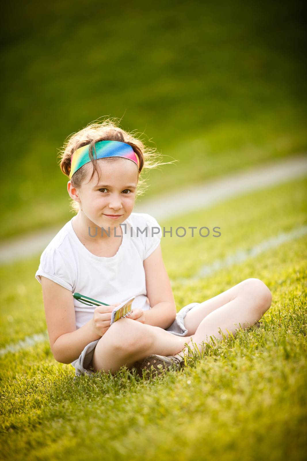 Little girl writing outside on the grass at the golden hour