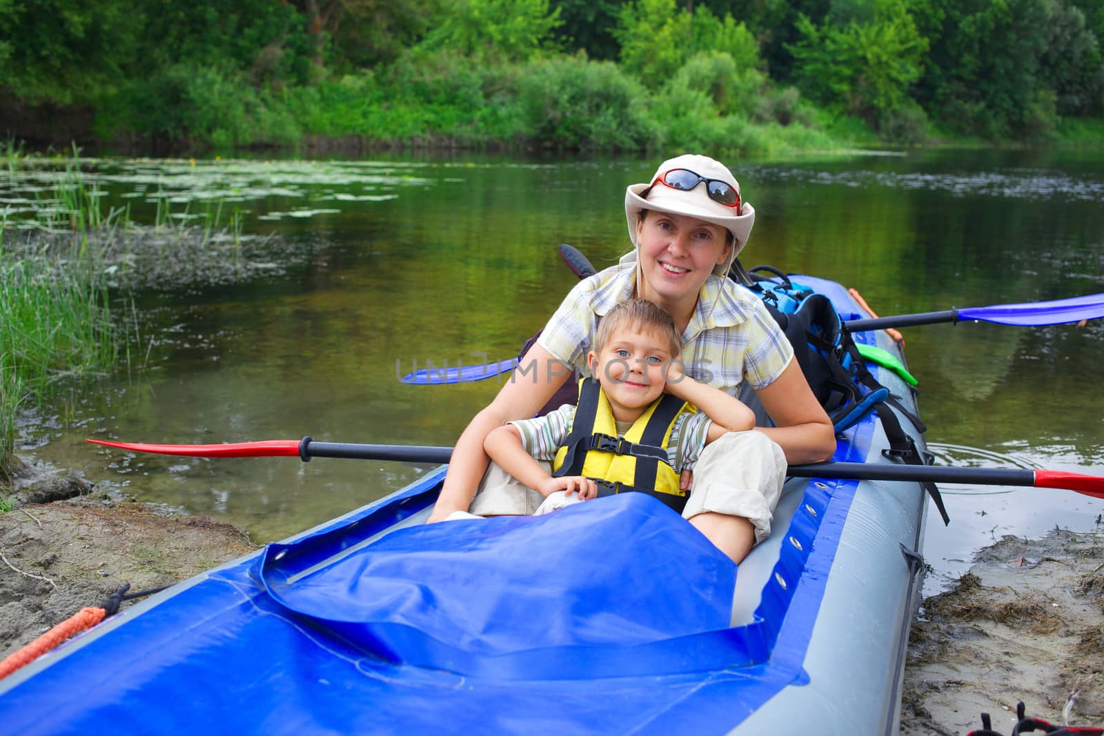Happy young boy with mother paddling a kayak on the river, enjoying a lovely summer day