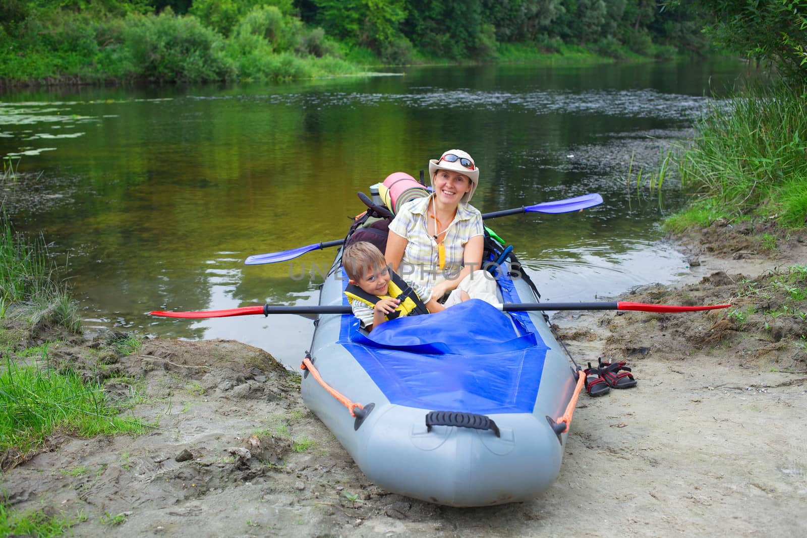 Happy young boy with mother paddling a kayak on the river, enjoying a lovely summer day