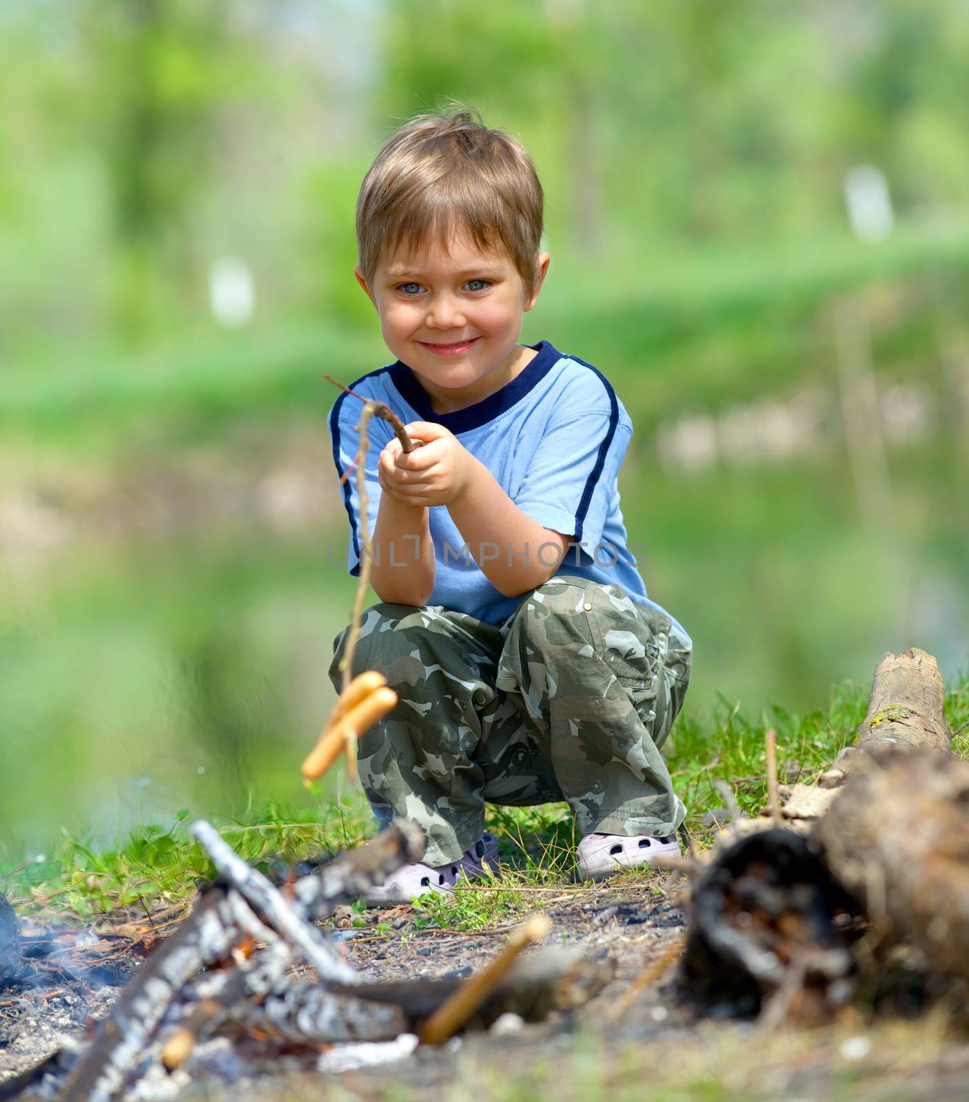 Cute boy cooking sausage by bonfire in hike.