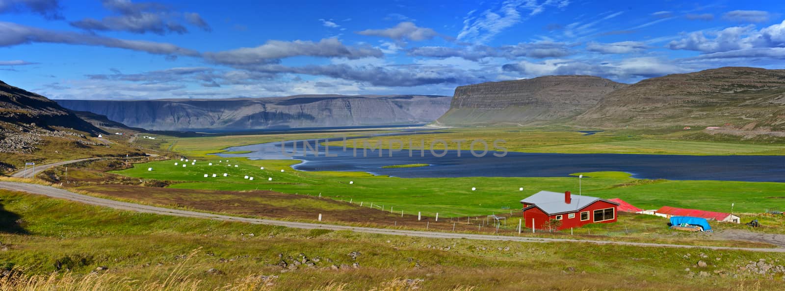 Beautiful red house in Iceland. Mountains, fjord, hay bales on the meadow in background. Panorama