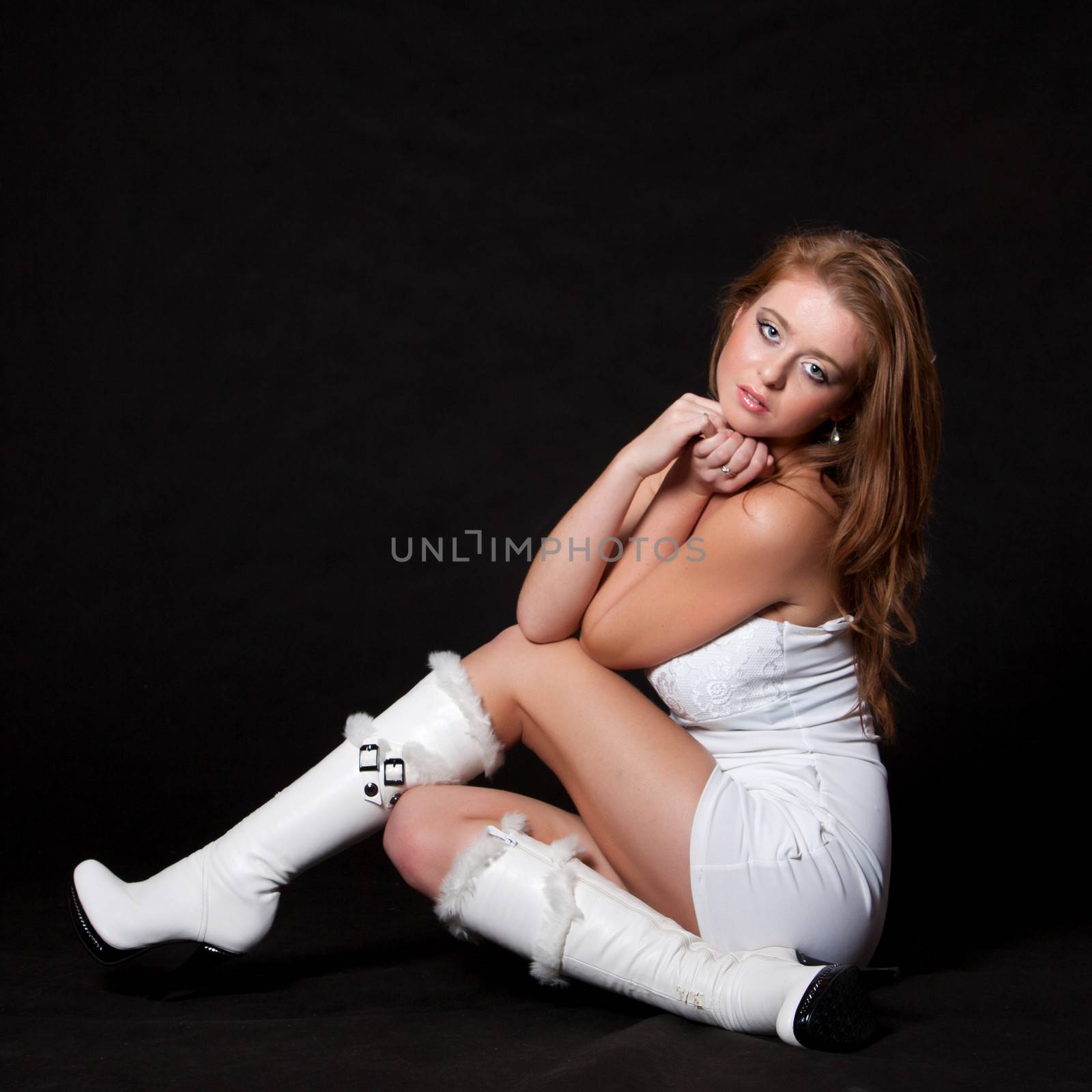 Young fashion model in a white mini dress sitting on the floor and looking up with a dreamy look on a black background