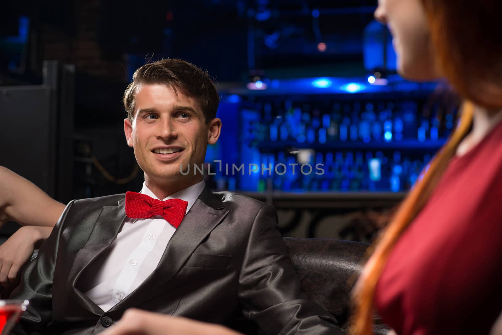 portrait of a man in a nightclub, sitting on the couch and talking with the woman, a date at a nightclub.