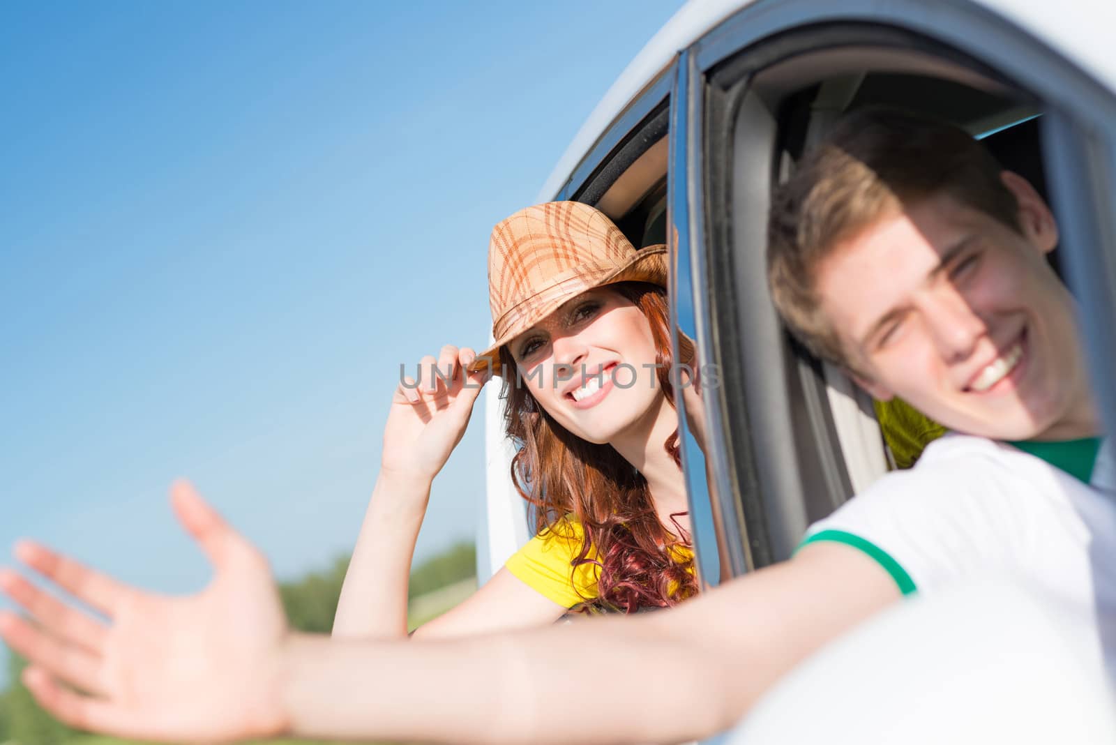 Young woman looking out of car window, holds the hand hat and smiling