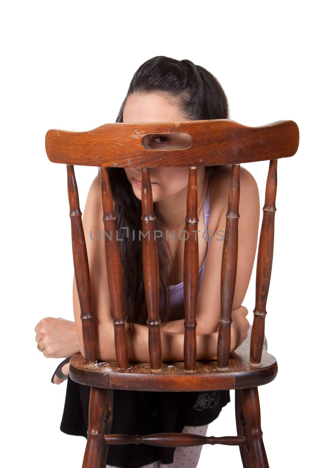 Long-haired brunette woman relies on a chair, is hidden; looking with one eye, isolated on a white background