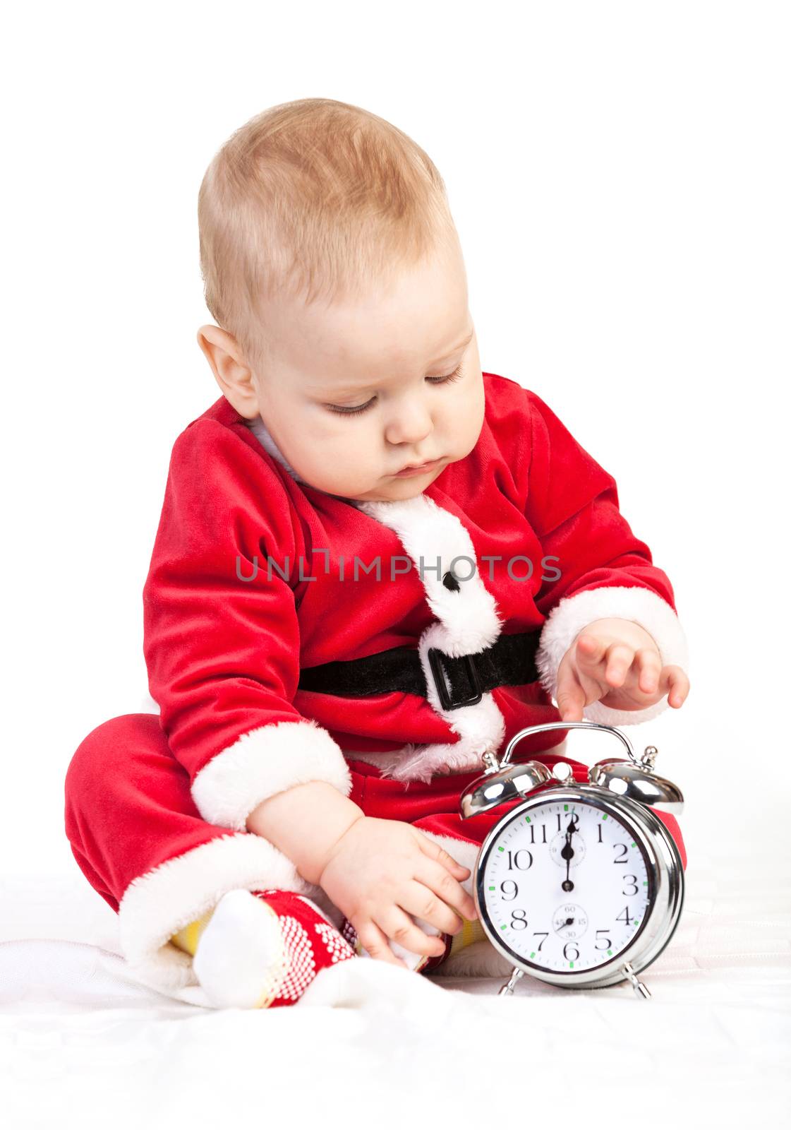 Cute little boy in Santa costume playing with alarm clock on white background