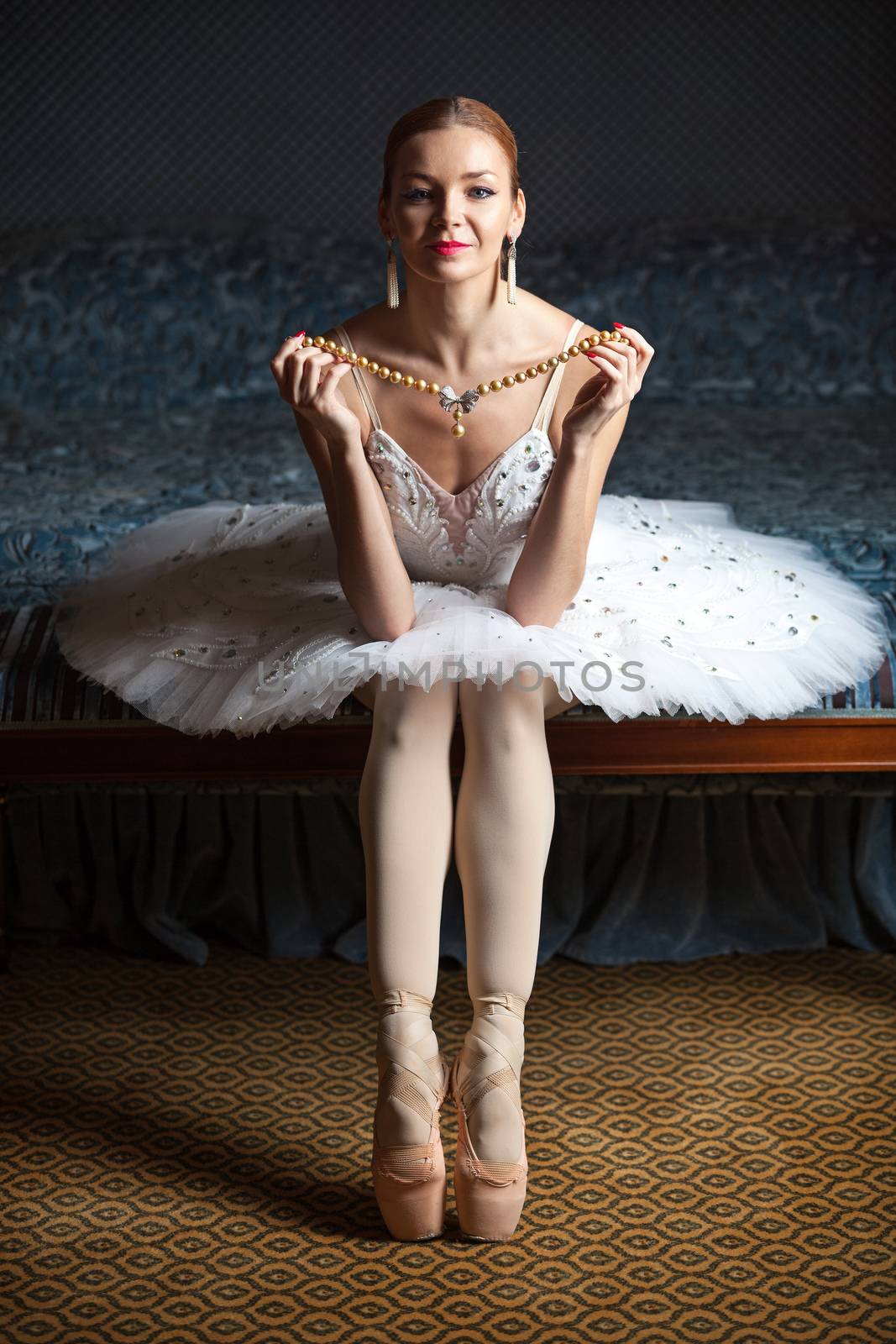 Ballerina holding pearl necklace and smiling in luxury interior