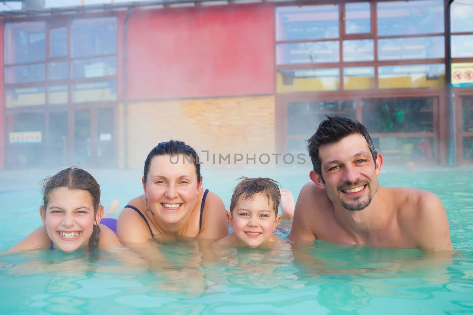 Activities on the pool. Portrait of happy family of four relaxing in termal swimming pool