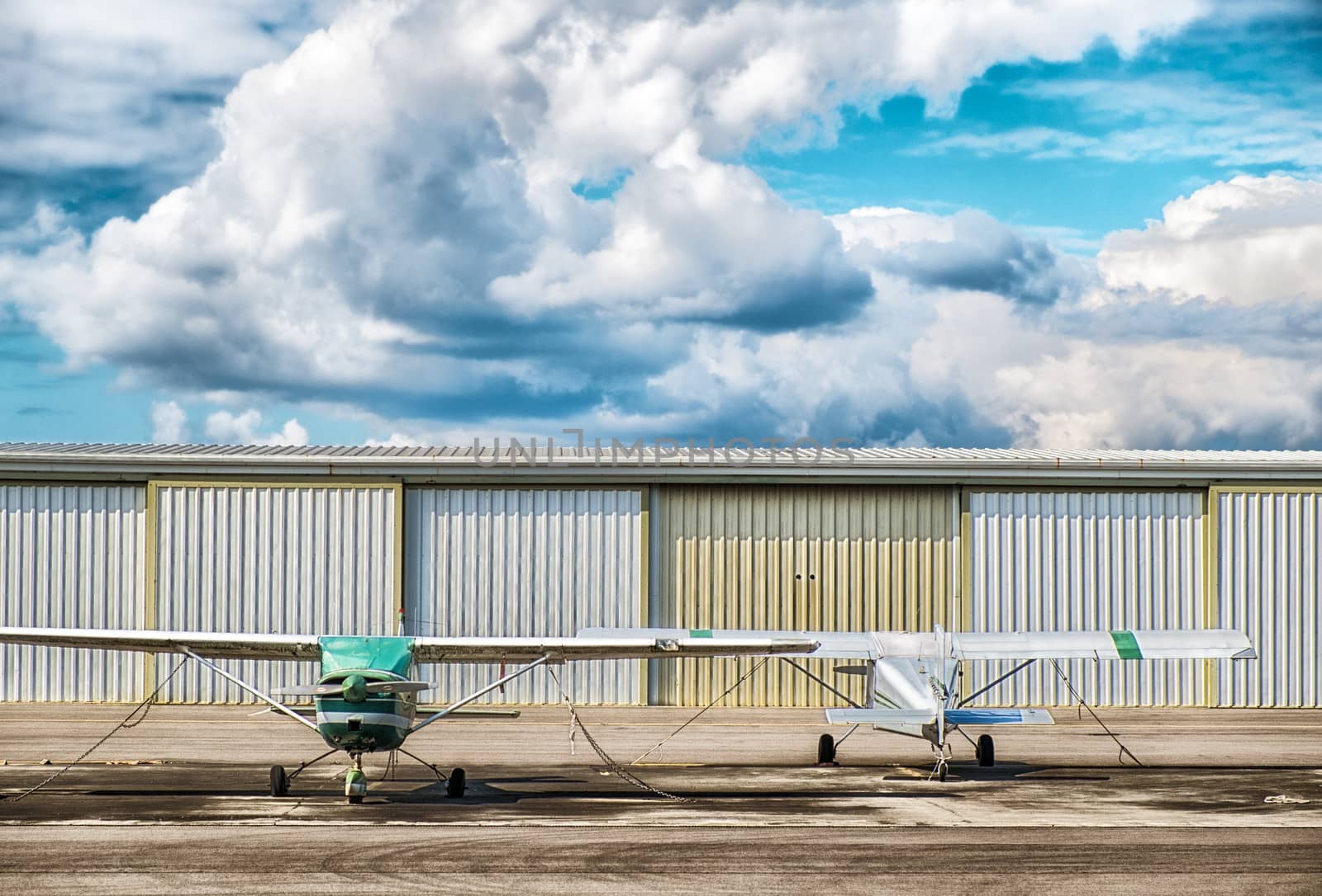 two small airplaines, clouds and hanger behind