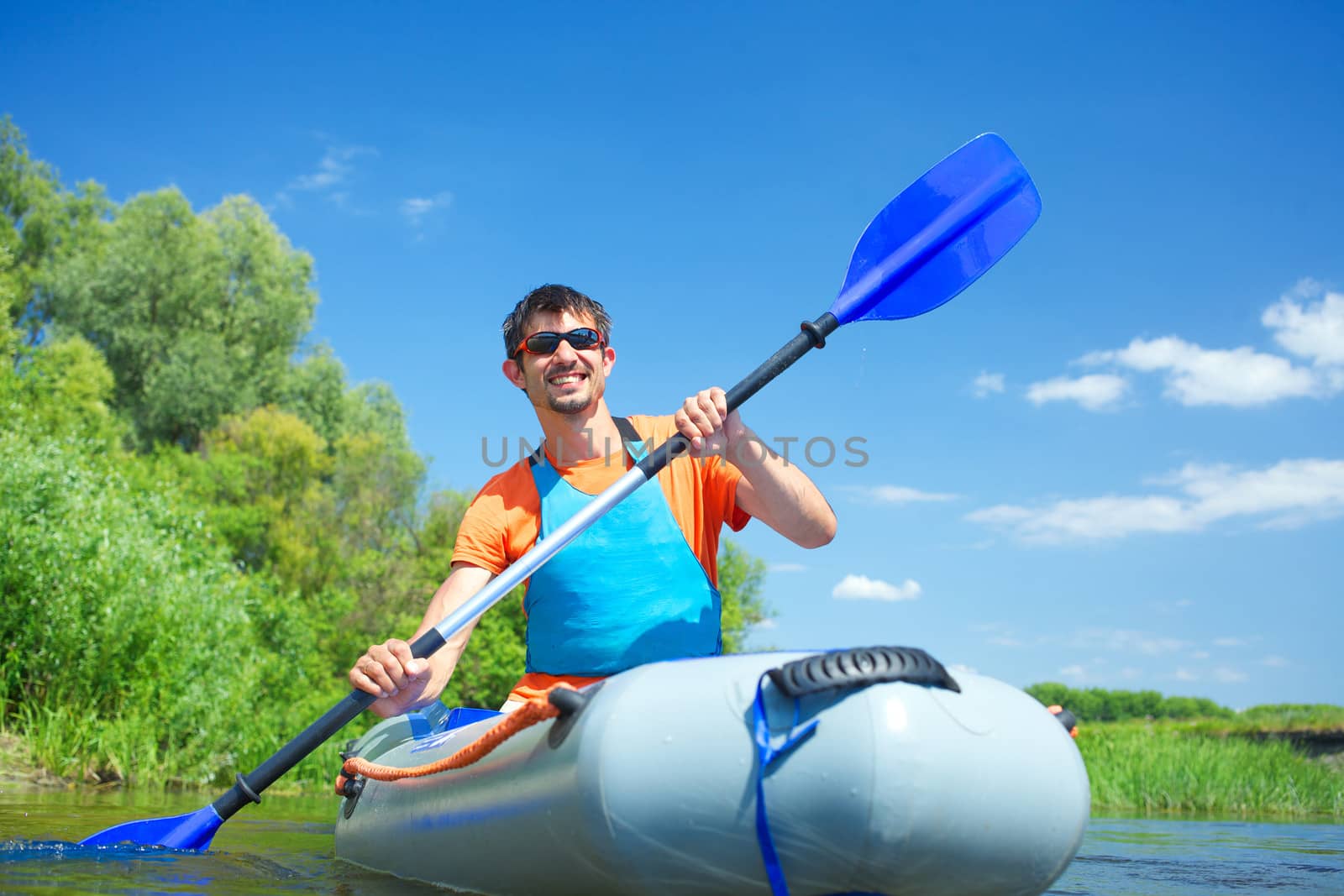Handsome man paddling a kayak on the river, enjoying a lovely summer day