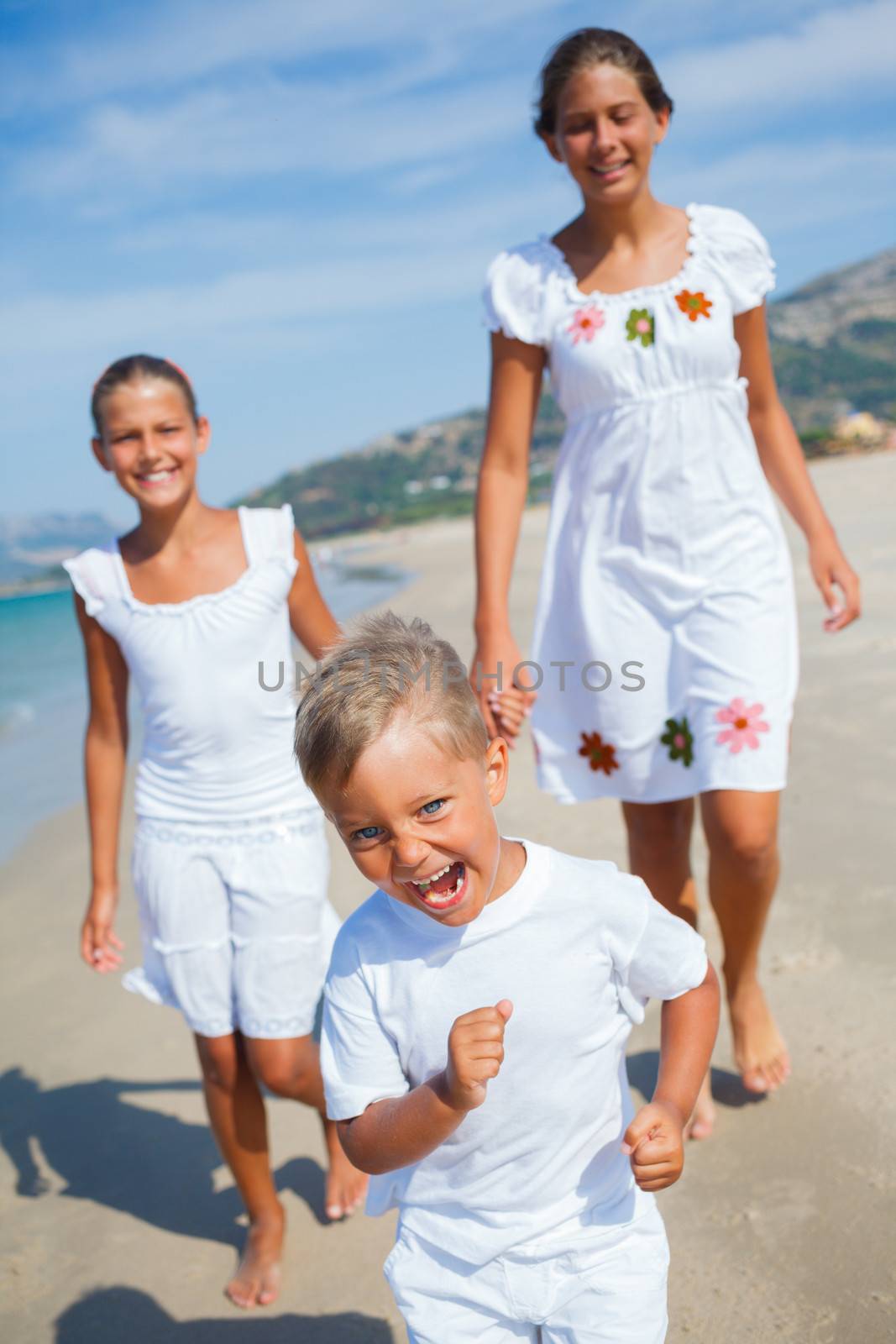 Adorable happy boy with his sisters running on beach vacation