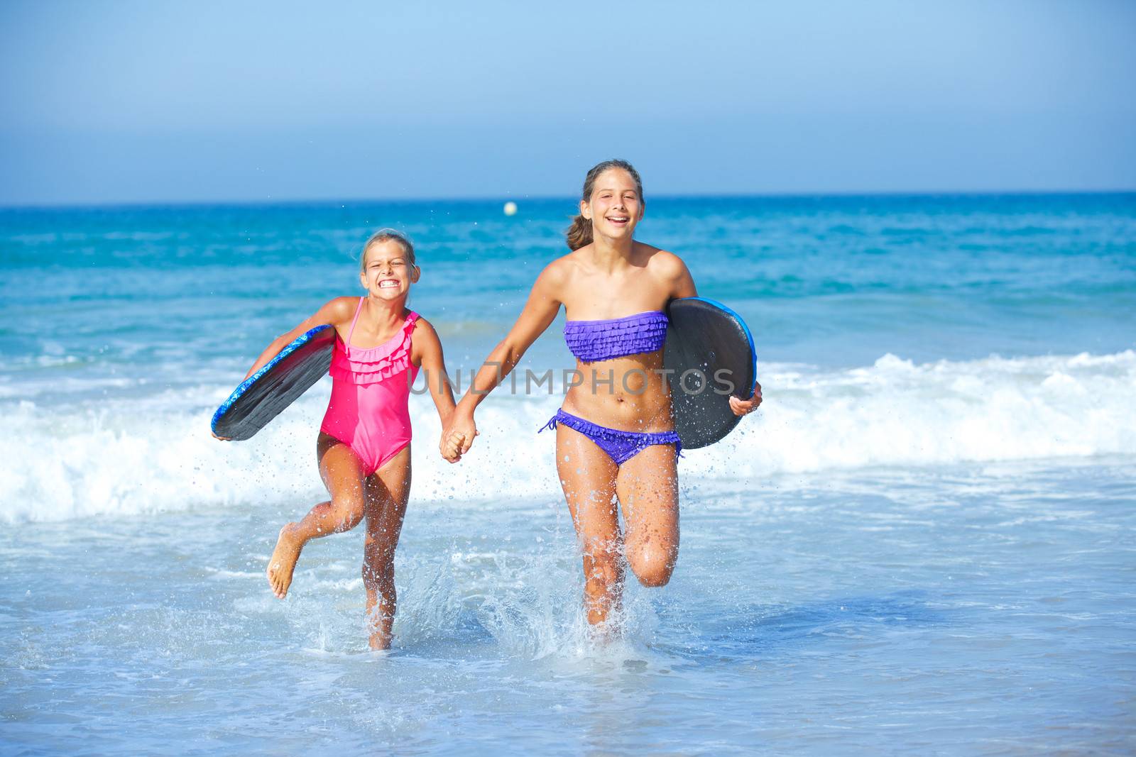 Summer vacation - Two cute girls in bikini with surfboard running from the ocean.