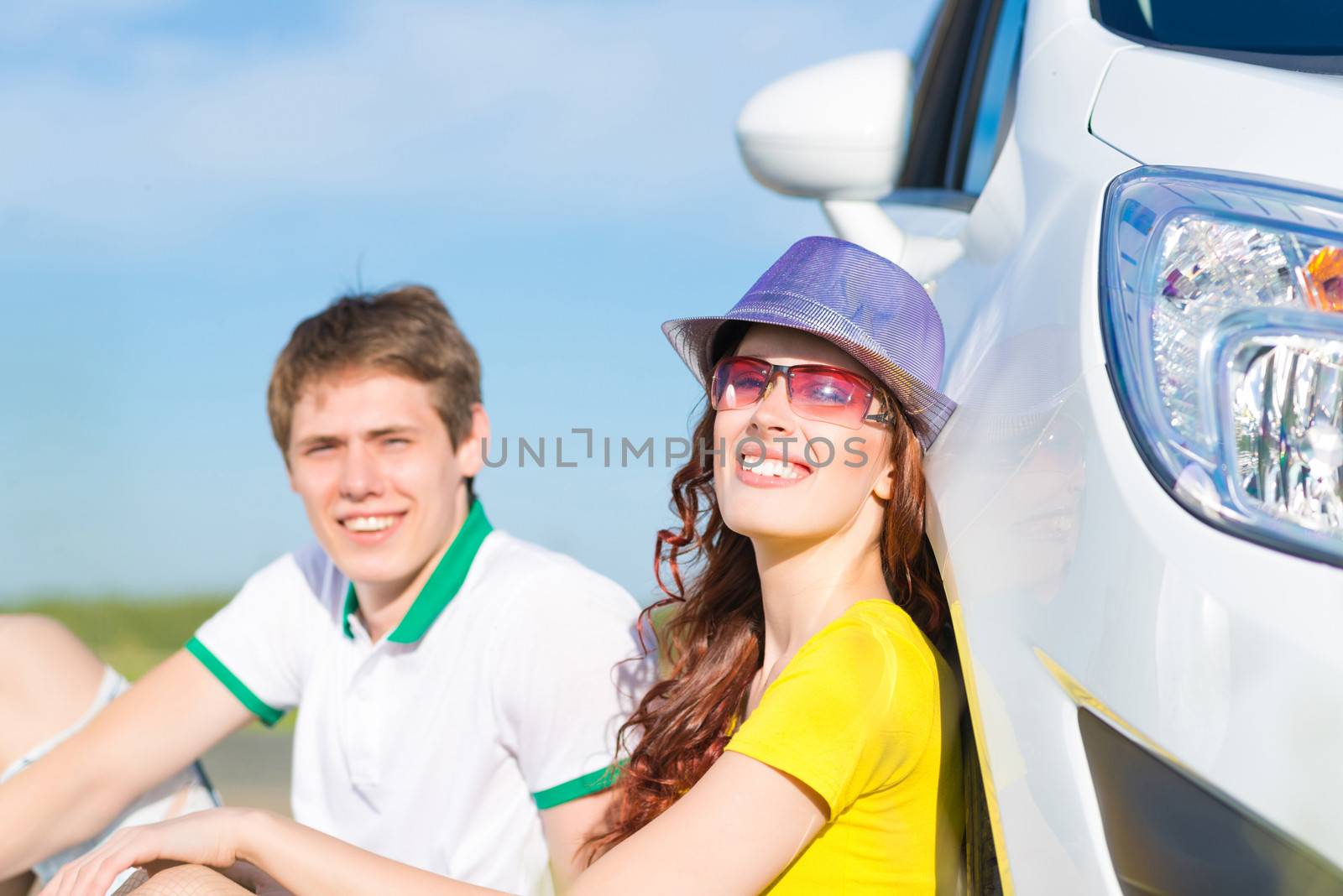 young couple sitting on the ground next to the wheel of a car, a summer road trip