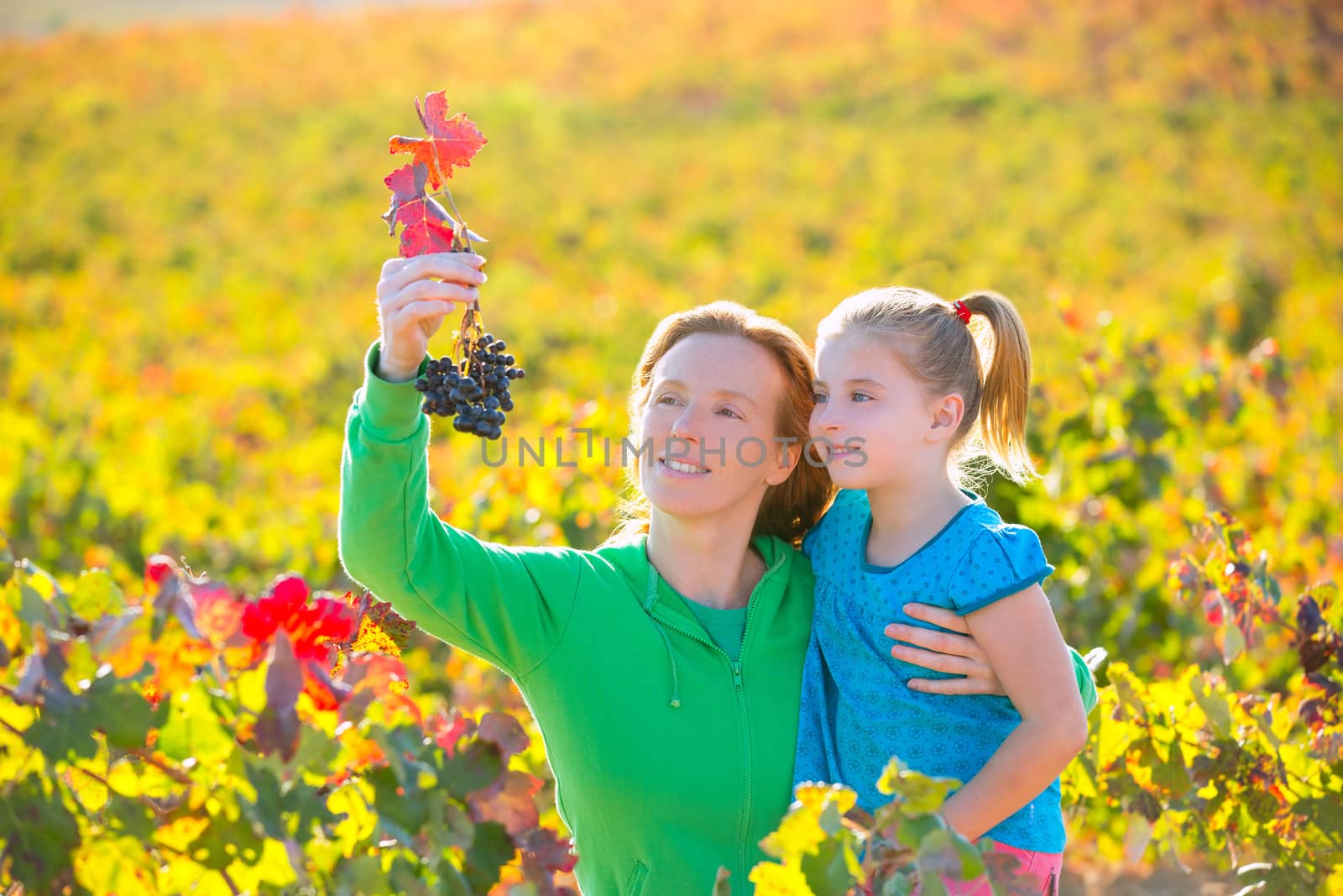 Mother and daughter on autumn vineyard smiling holding grape by lunamarina