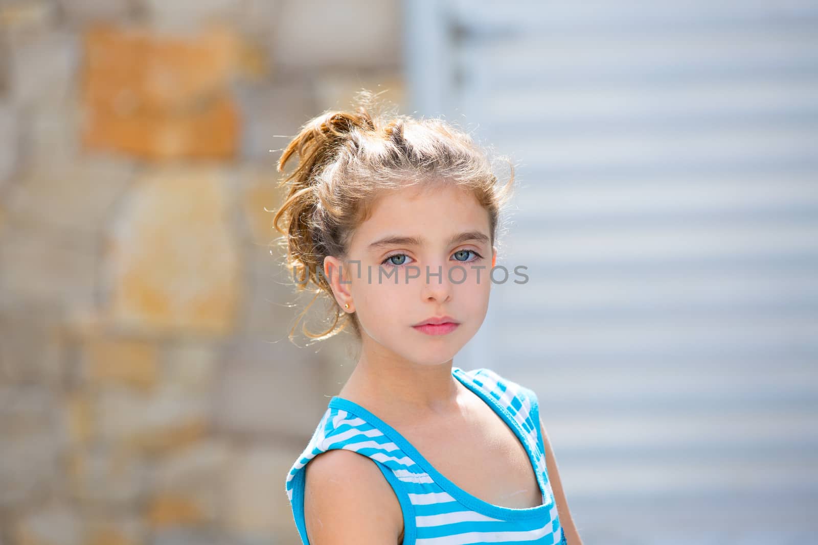 Beautiful kid girl portrait in blue with stones and door in blur background