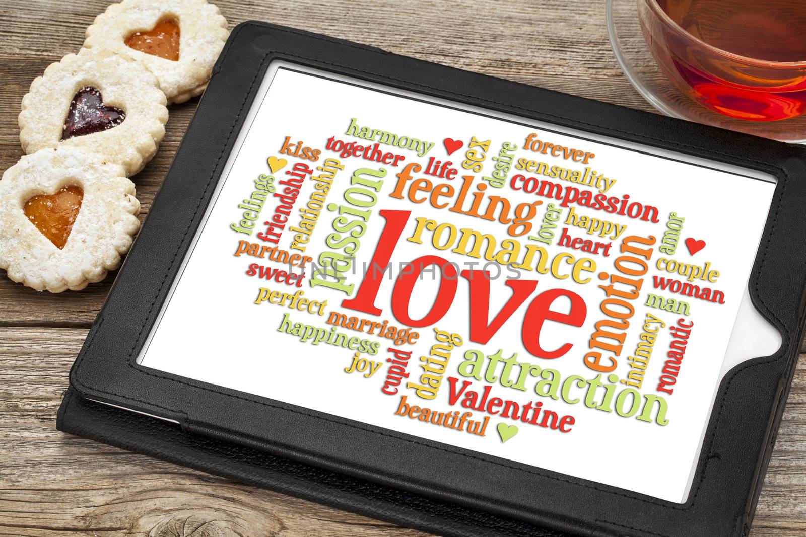 love word cloud on a digital tablet screen with heart cookies and a cup of tea